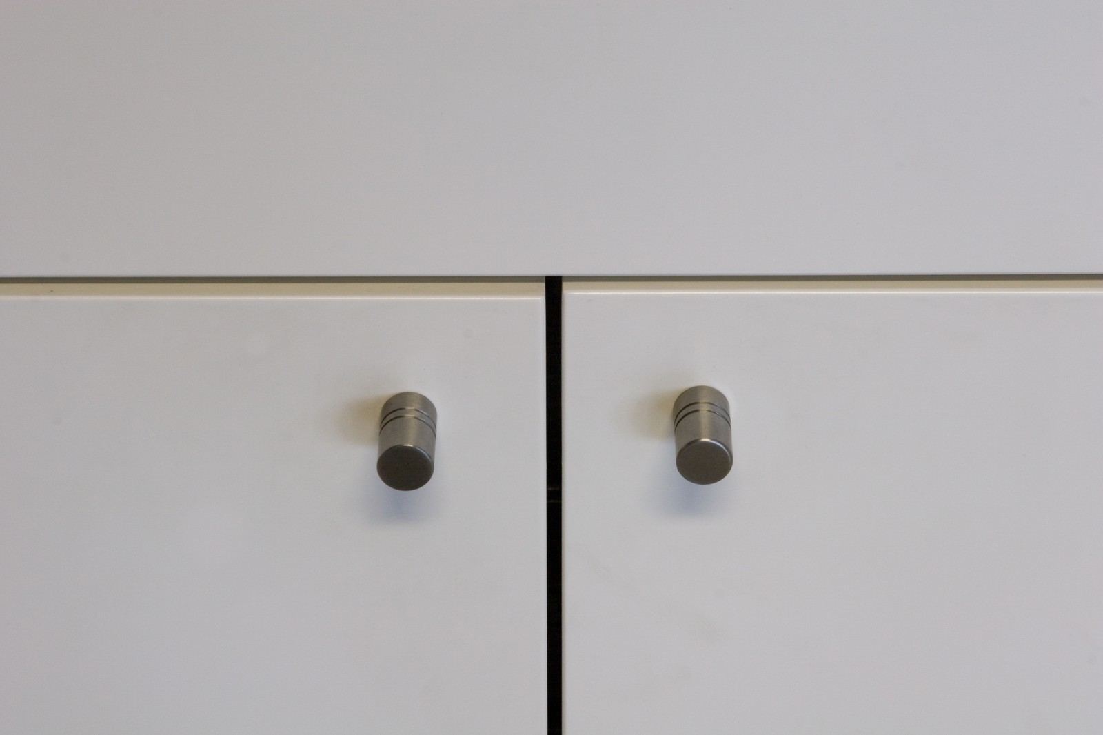 Detail van twee aluminium knoppen op witte kastdeuren.