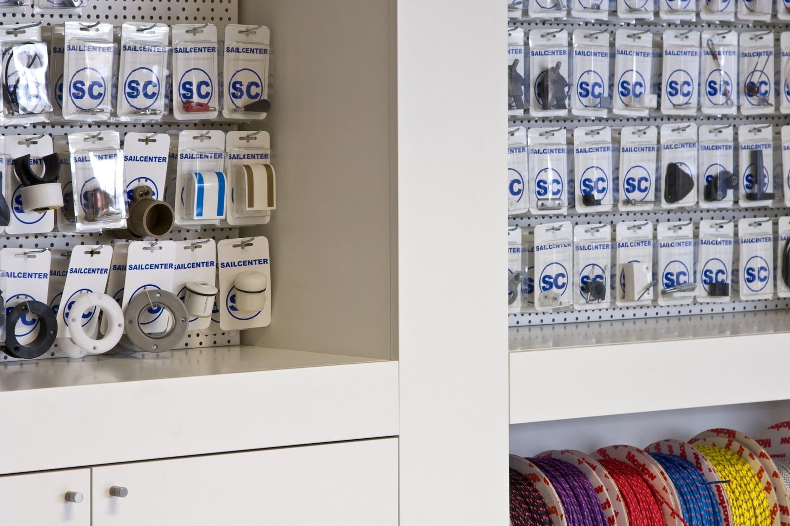 Kast met pegboardvakken vol accessoires boven kleurrijke touwspoelen.