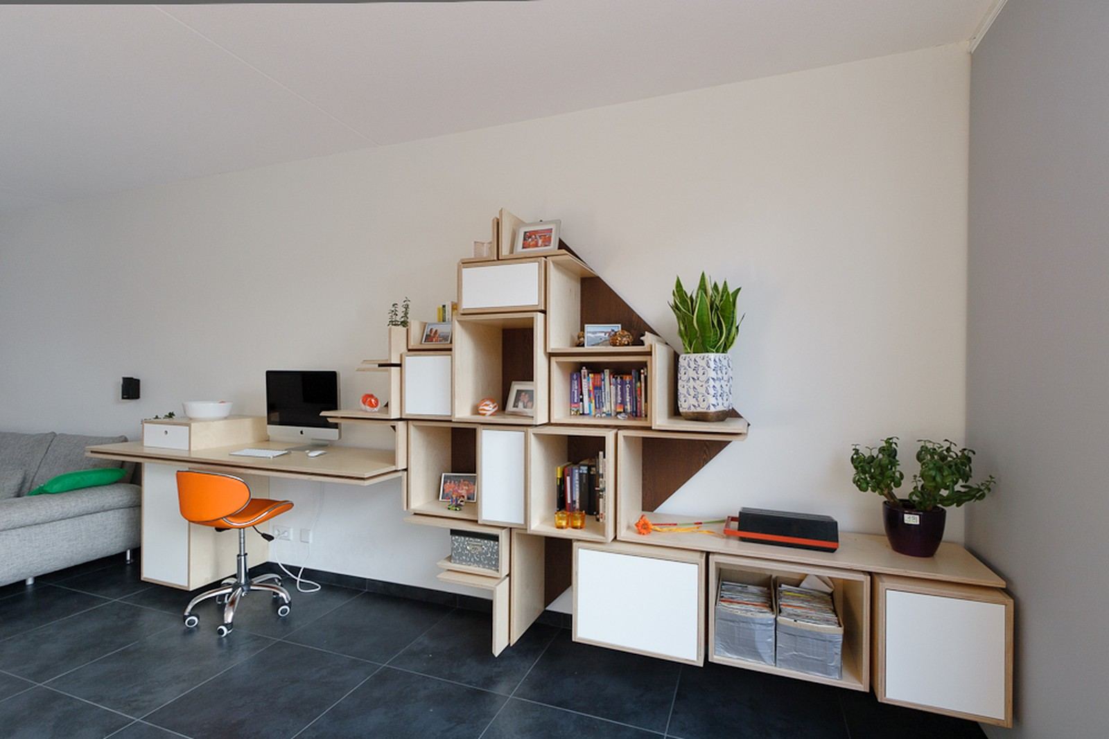 Bureau dat aansluit op een puzzelvormige wandkast met vakken in verschillende maten.