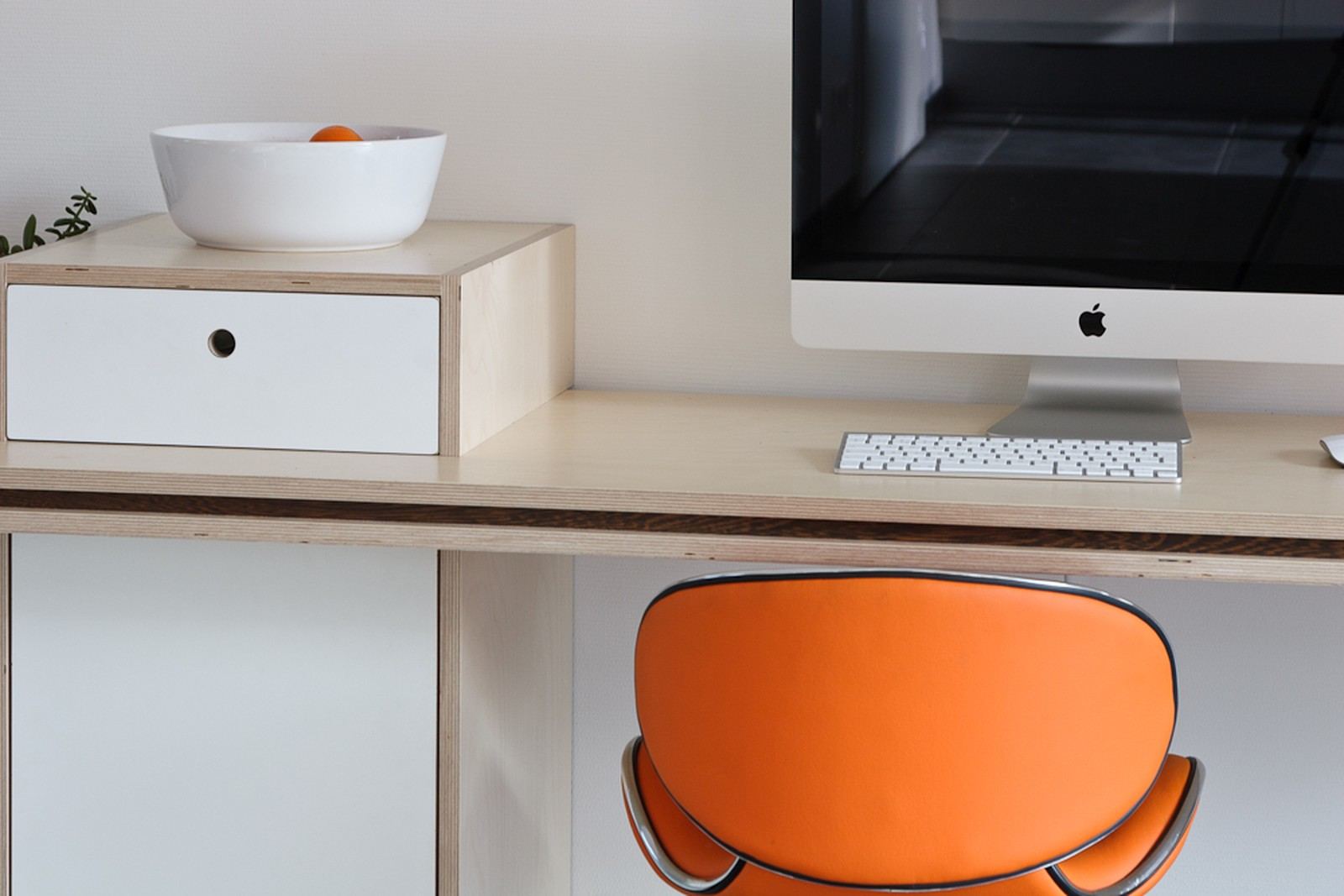 Bureau van licht hout met een donkere accentstrook, met een oranje stoel eronder.