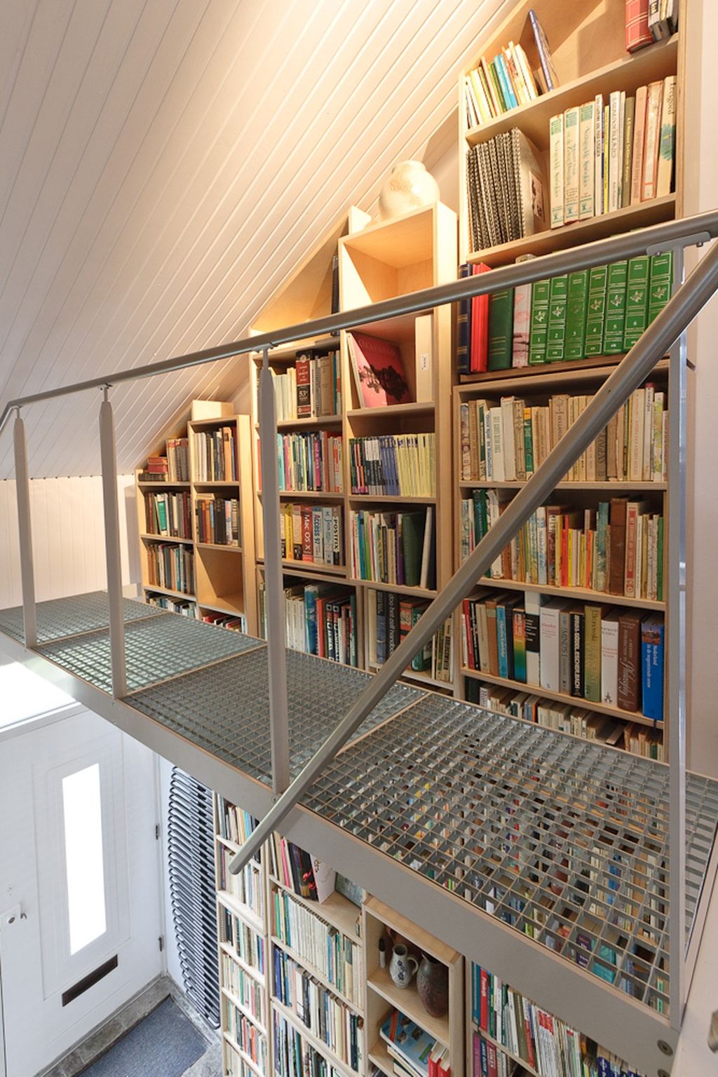 Boekenkast die tot aan de nok reikt, met een stalen loopbrug ervoor.