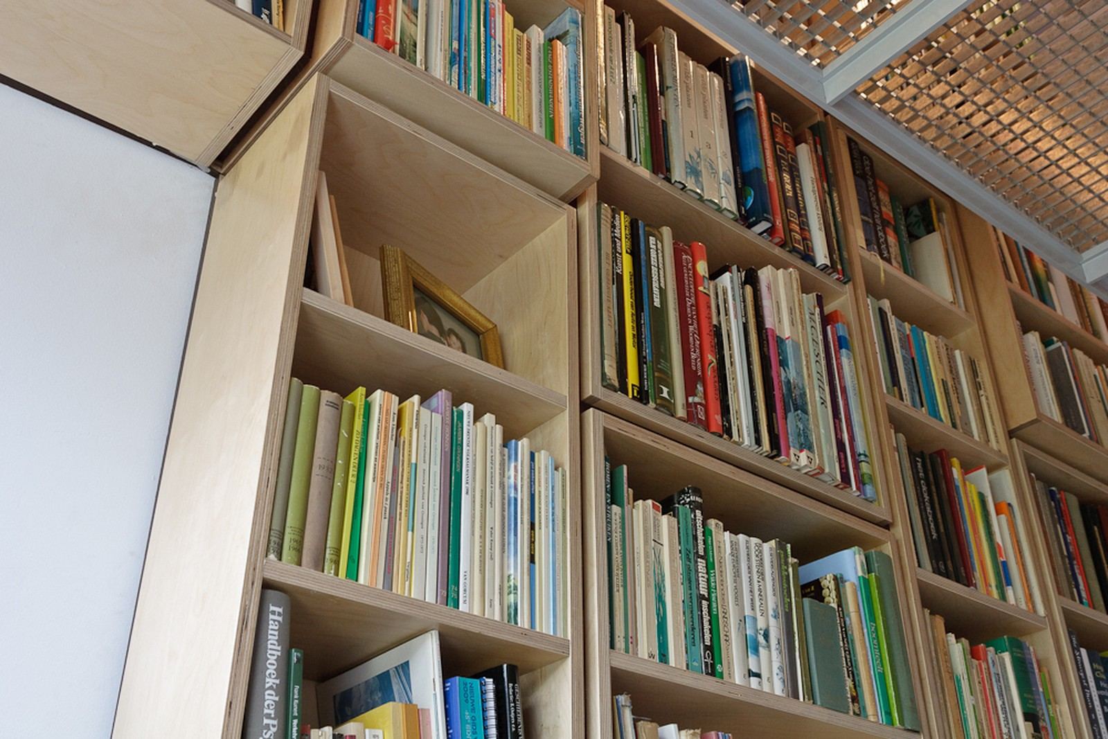 Boekenkast die schuin oploopt langs de dakhelling, met een raster van vakken.