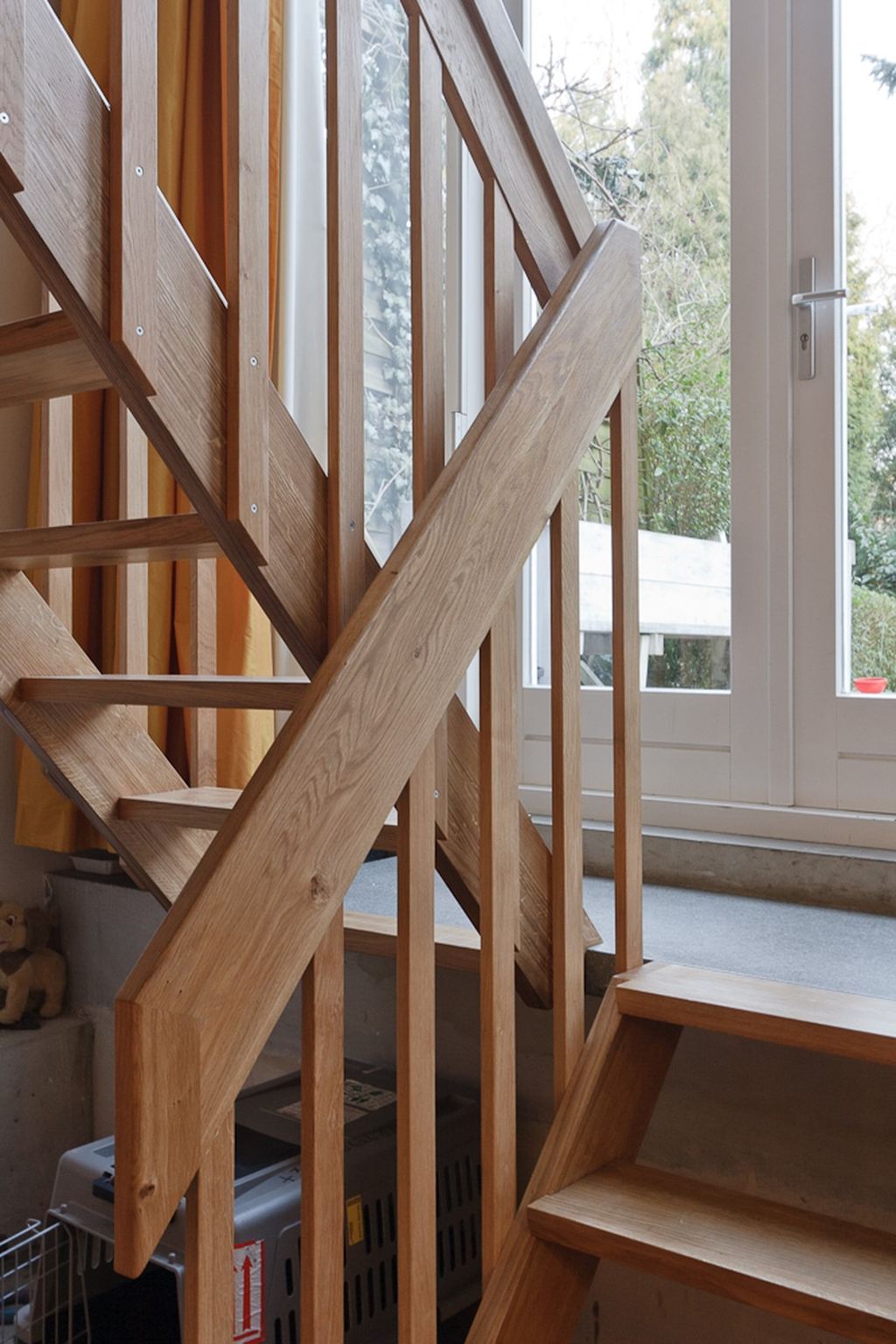 Detail van de gekruiste eikenhouten trapleuning bij het raam.