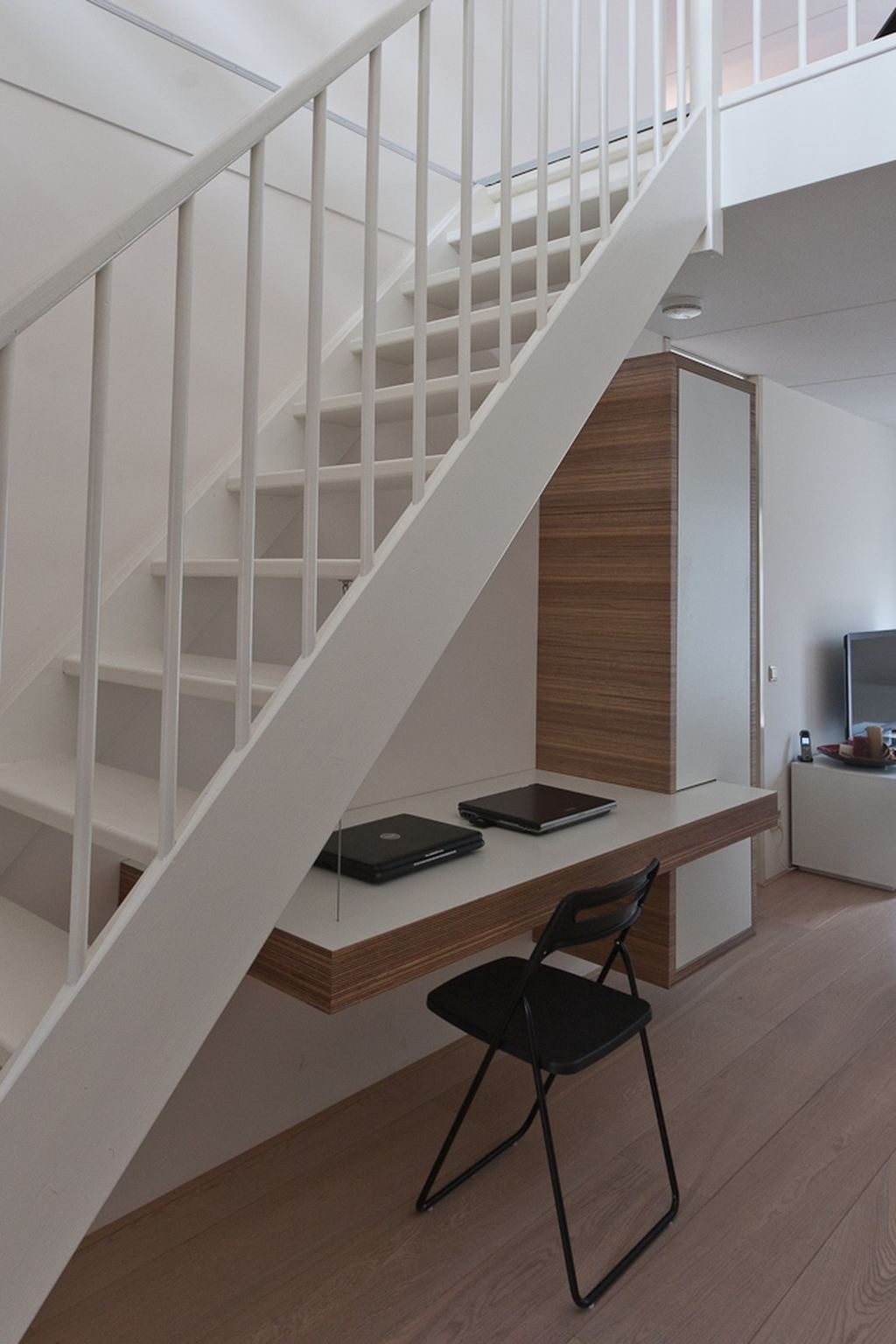Zwevend bureau met plexwood rand onder een trap, naast een kast.