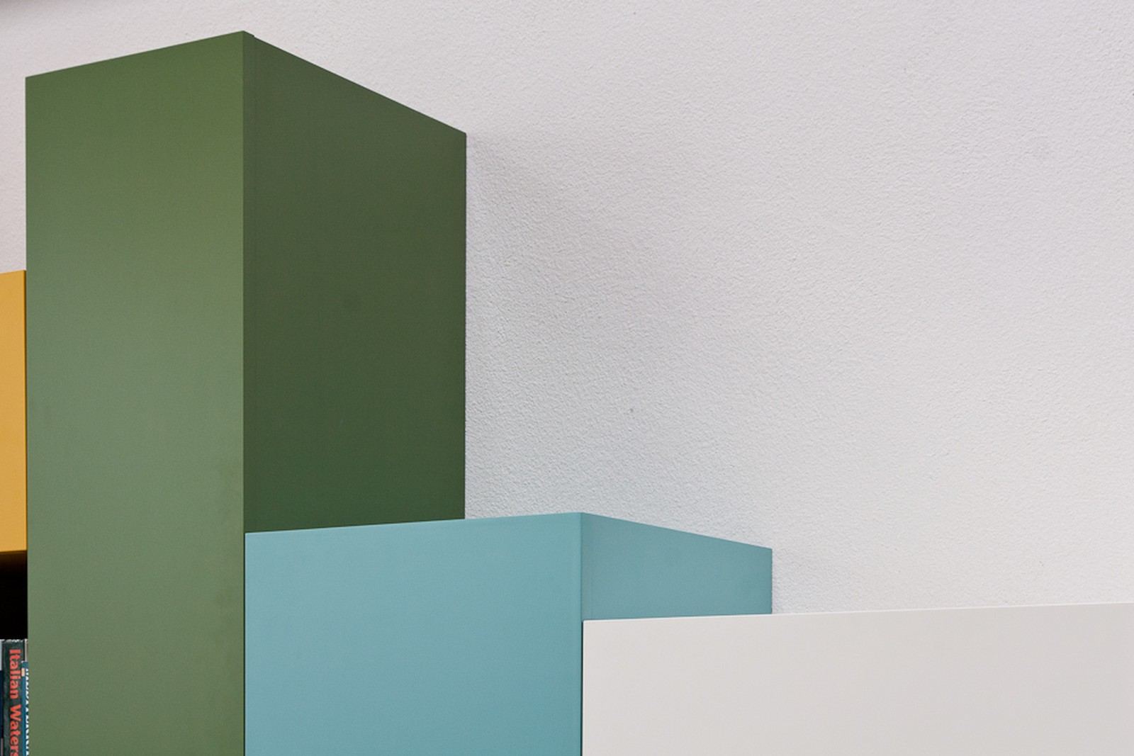 Detail van boeken in een vak tussen gele, grijze en witte kastblokken.