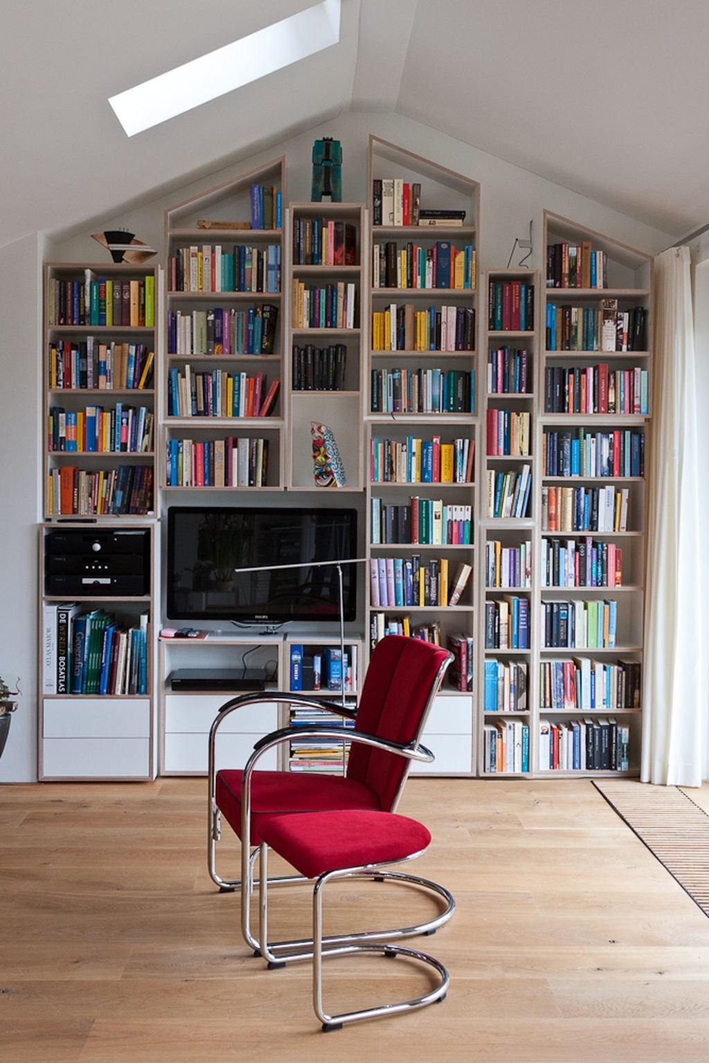 Verticale boekenkastelementen die de puntvorm van het dak volgen, met TV-meubel.