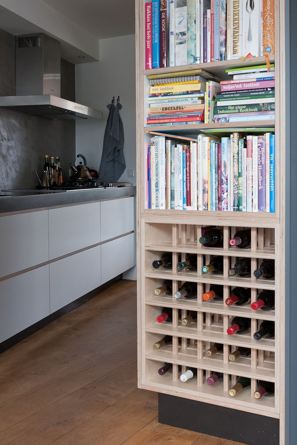 Hoge kast met open planken vol kookboeken boven een rooster met wijnflessen.