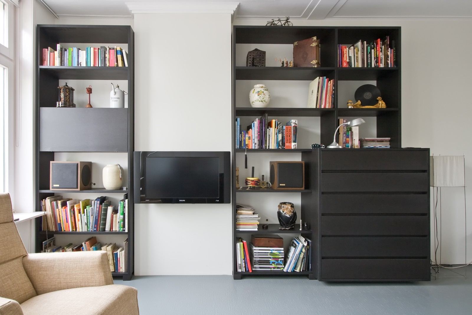 Zwarte boekenkasten met open achterwand aan weerszijden van de televisie.