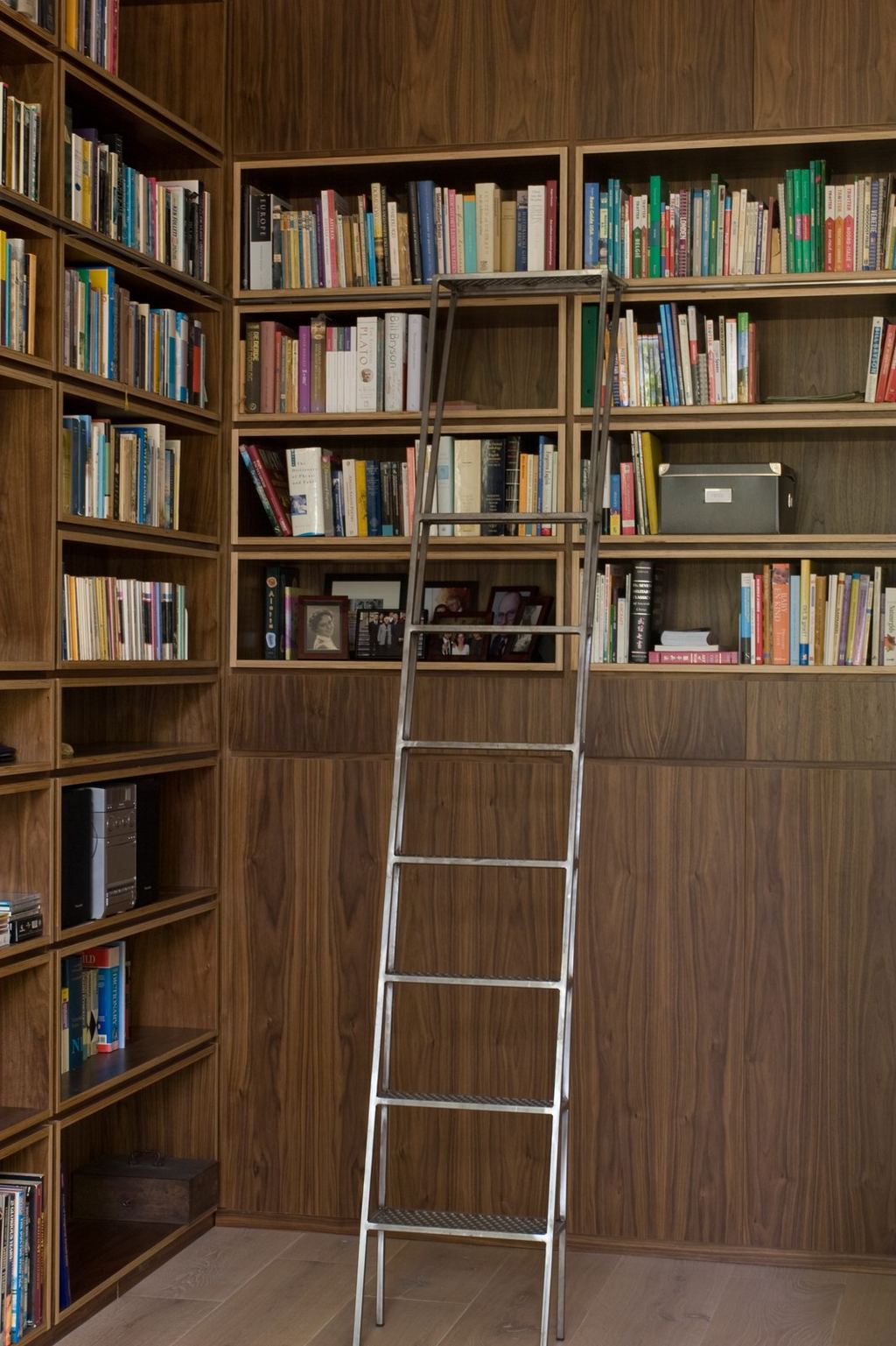Wandvullende notenfineer boekenkast met een stalen rolladder ervoor.