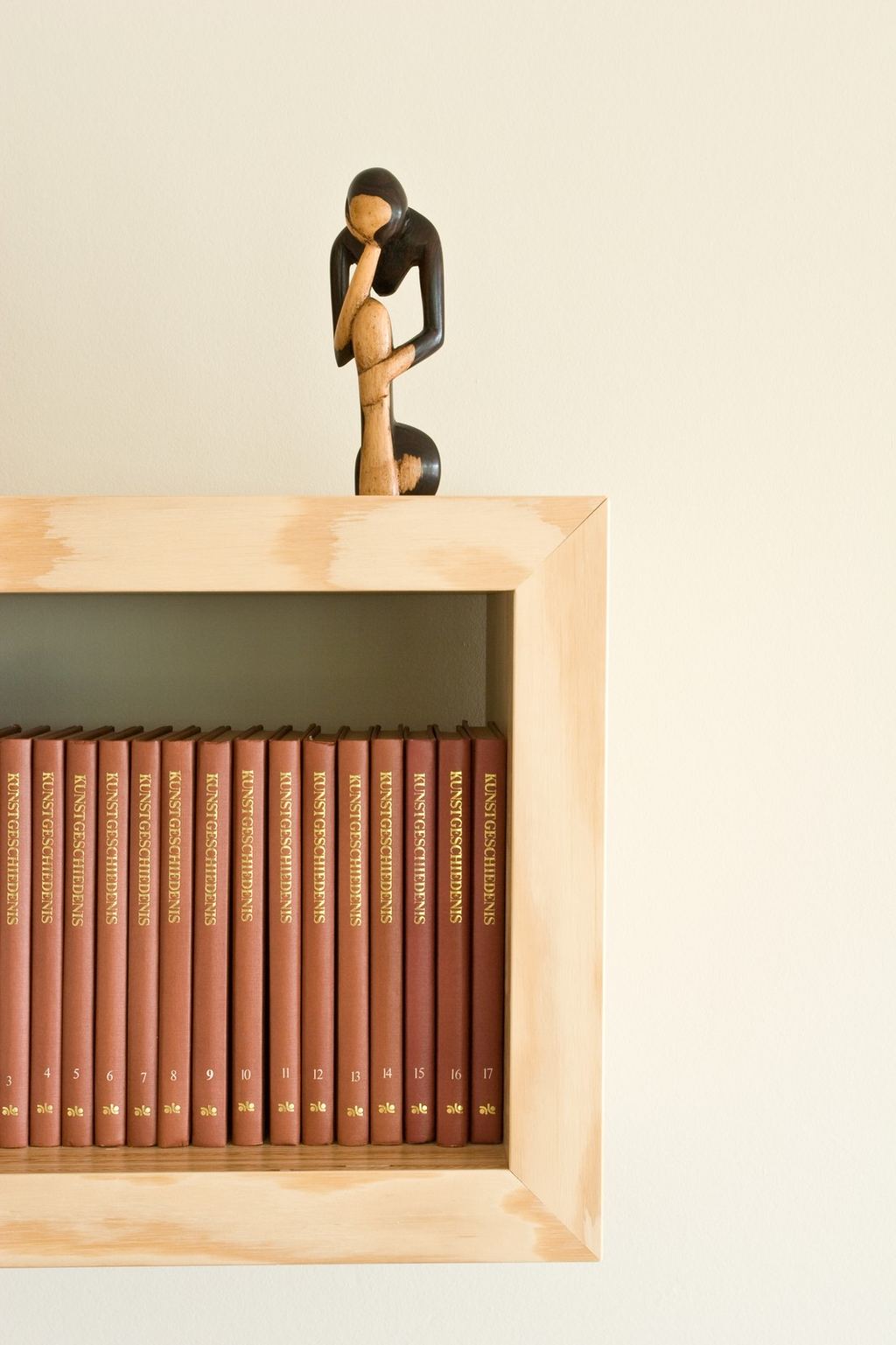 Rij encyclopedieën met een houten beeldje bovenop de plank.