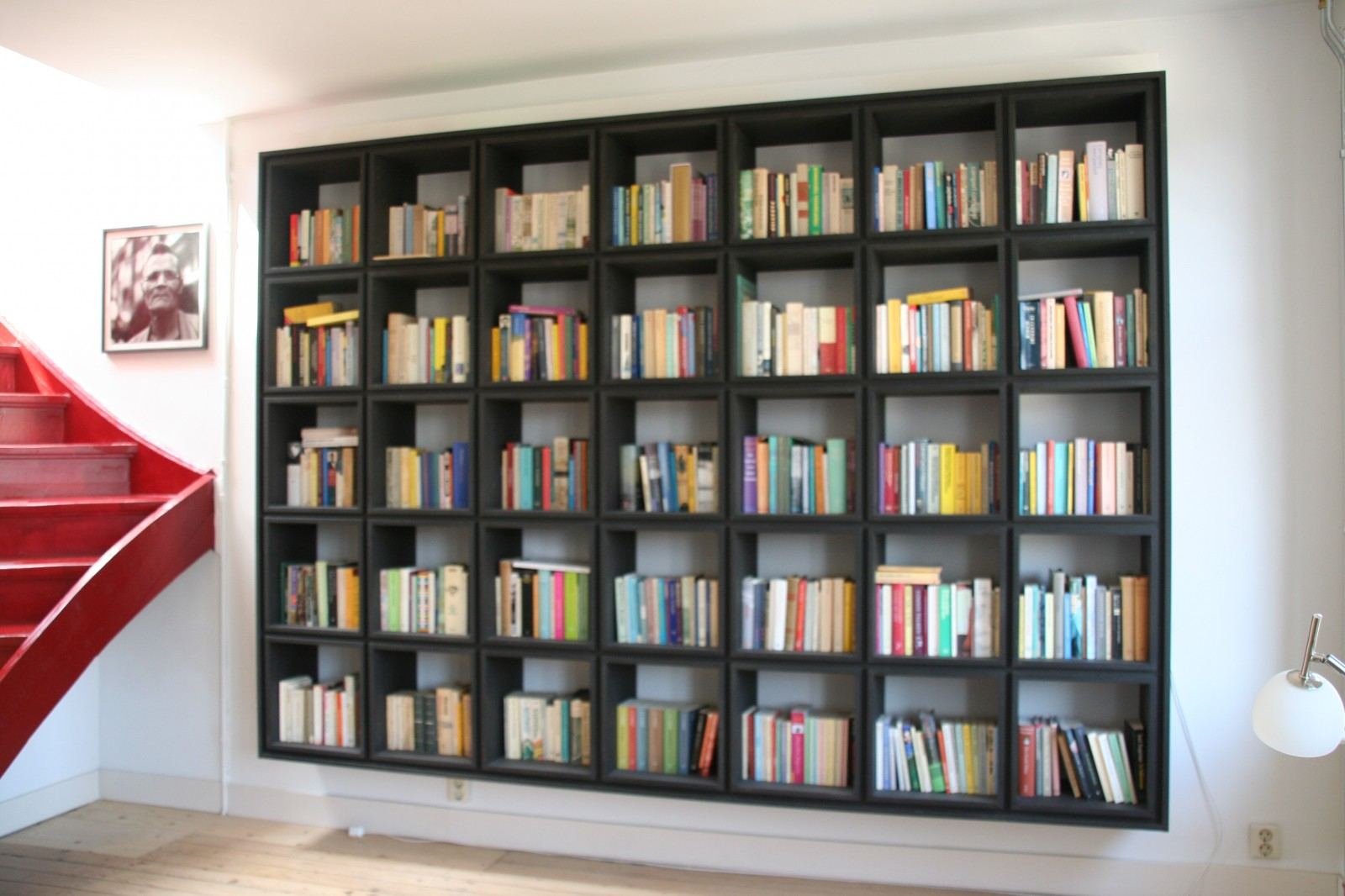 Zwarte boekenkast met een raster van vakken, volledig gevuld met kleurrijke boeken.