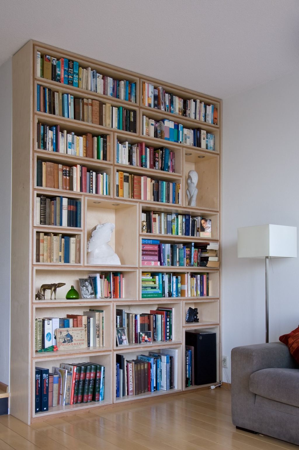 Wandvullende boekenkast van berken multiplex met een asymmetrisch vakkenraster.