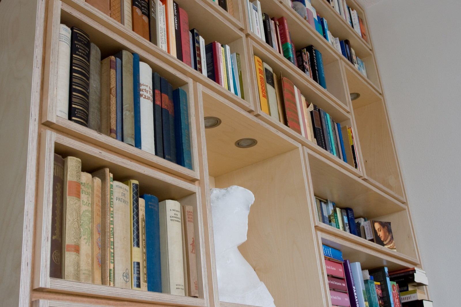 Schuin gefotografeerd deel van de boekenkast met een stenen beeld.