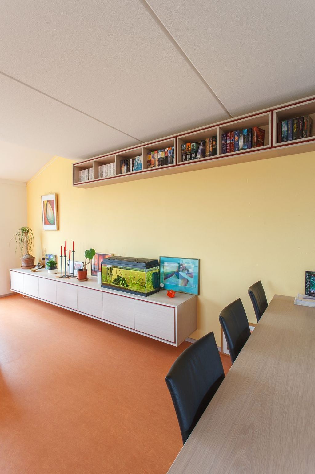 Dressoir met rode rand onder een lange wandkast vol boeken.