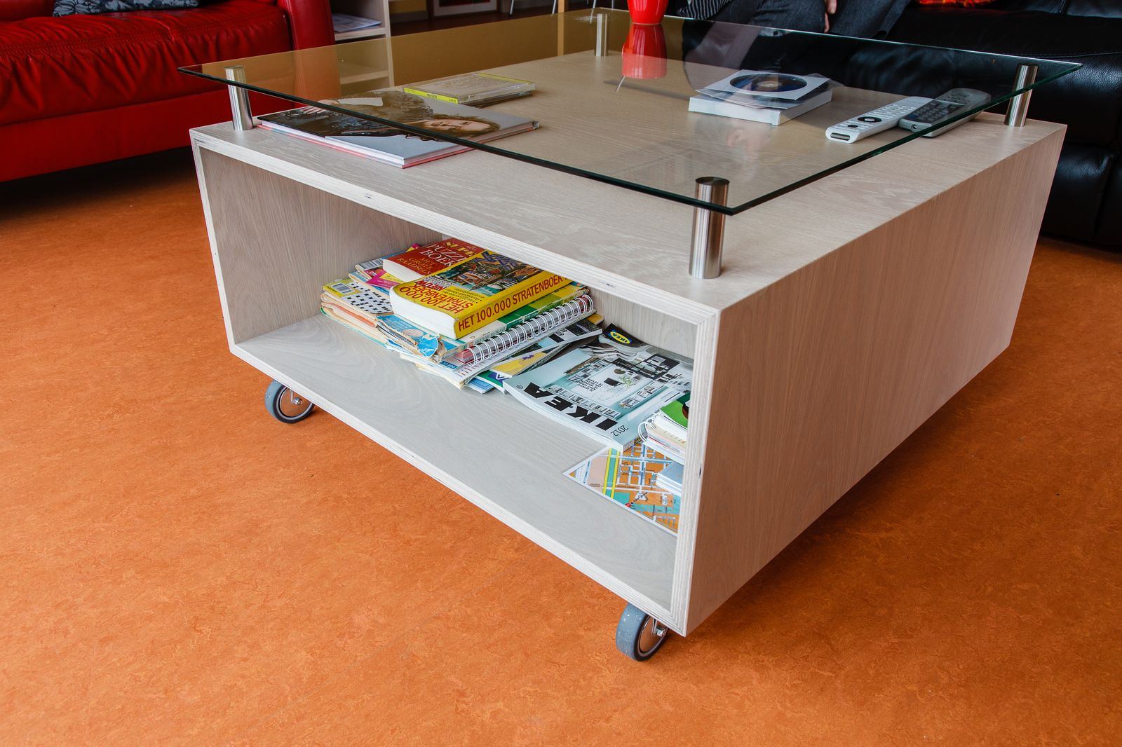 Salontafel op wielen met glazen blad en open opbergvak.