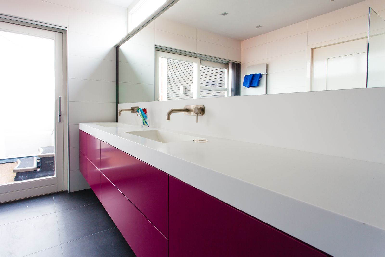 Zwevend badkamermeubel in magenta op een ronde metalen voet, met een spiegel erboven.