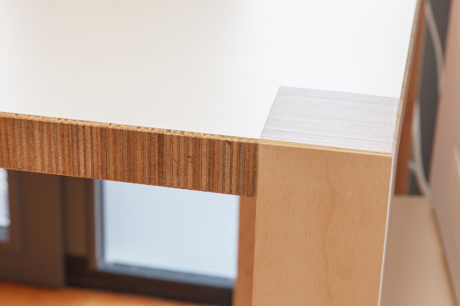 Detail van een werkblad in wit HPL met een poot in berken multiplex.