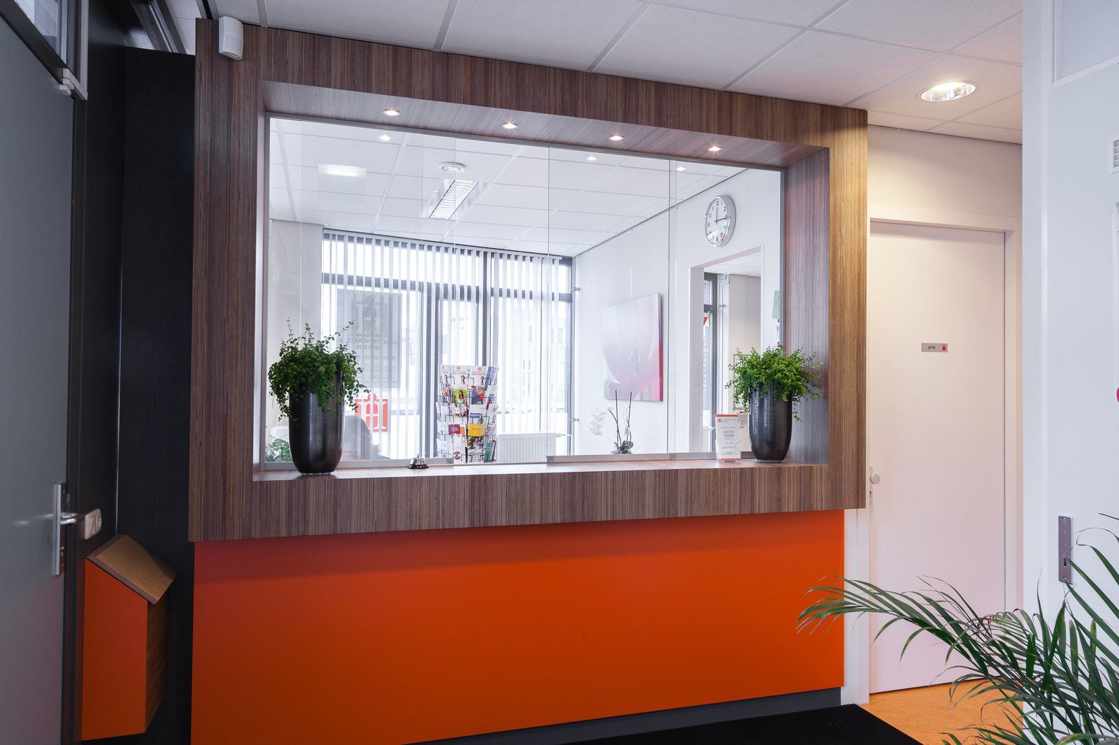 Balie met glazen doorkijk, ingelijst in donker plexwood en oranje HPL.