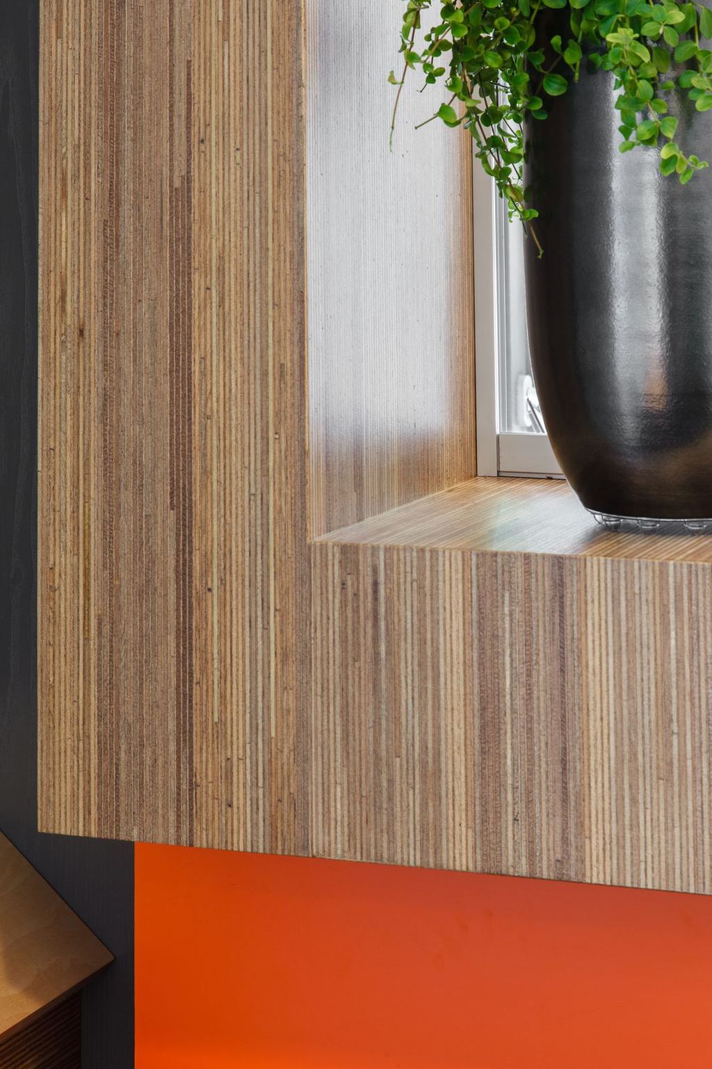 Detail van een vensterbank in meranti plexwood, boven een oranje kastfront.