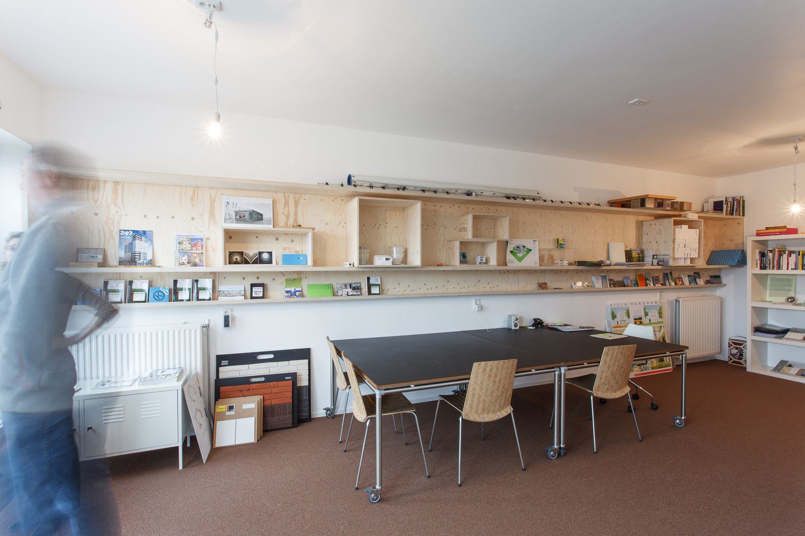 Lange wandkast van vuren multiplex met brochures en maquettes in een kantoor.