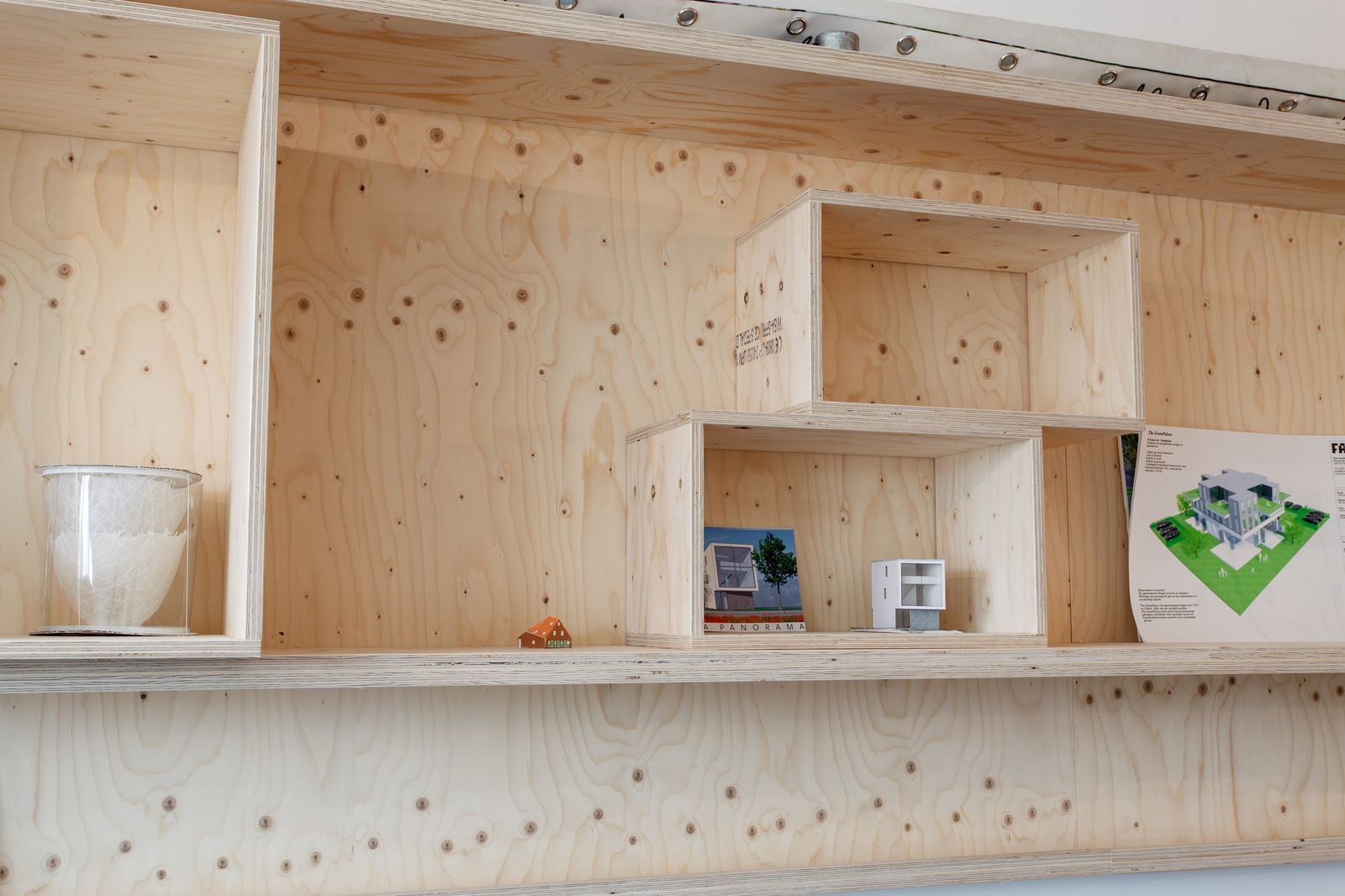 Open vakken van de wandkast met bouwmaquettes en tijdschriften.
