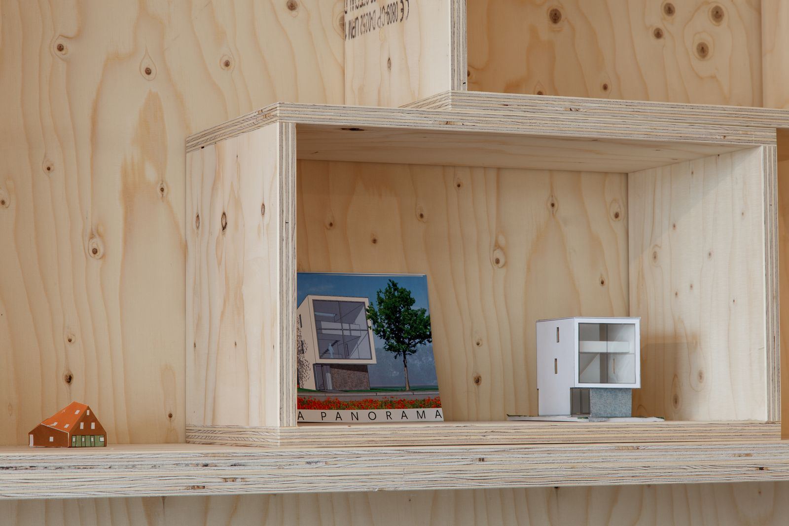 Vak met een miniatuurhuisje en architectuurbrochures op de plank.