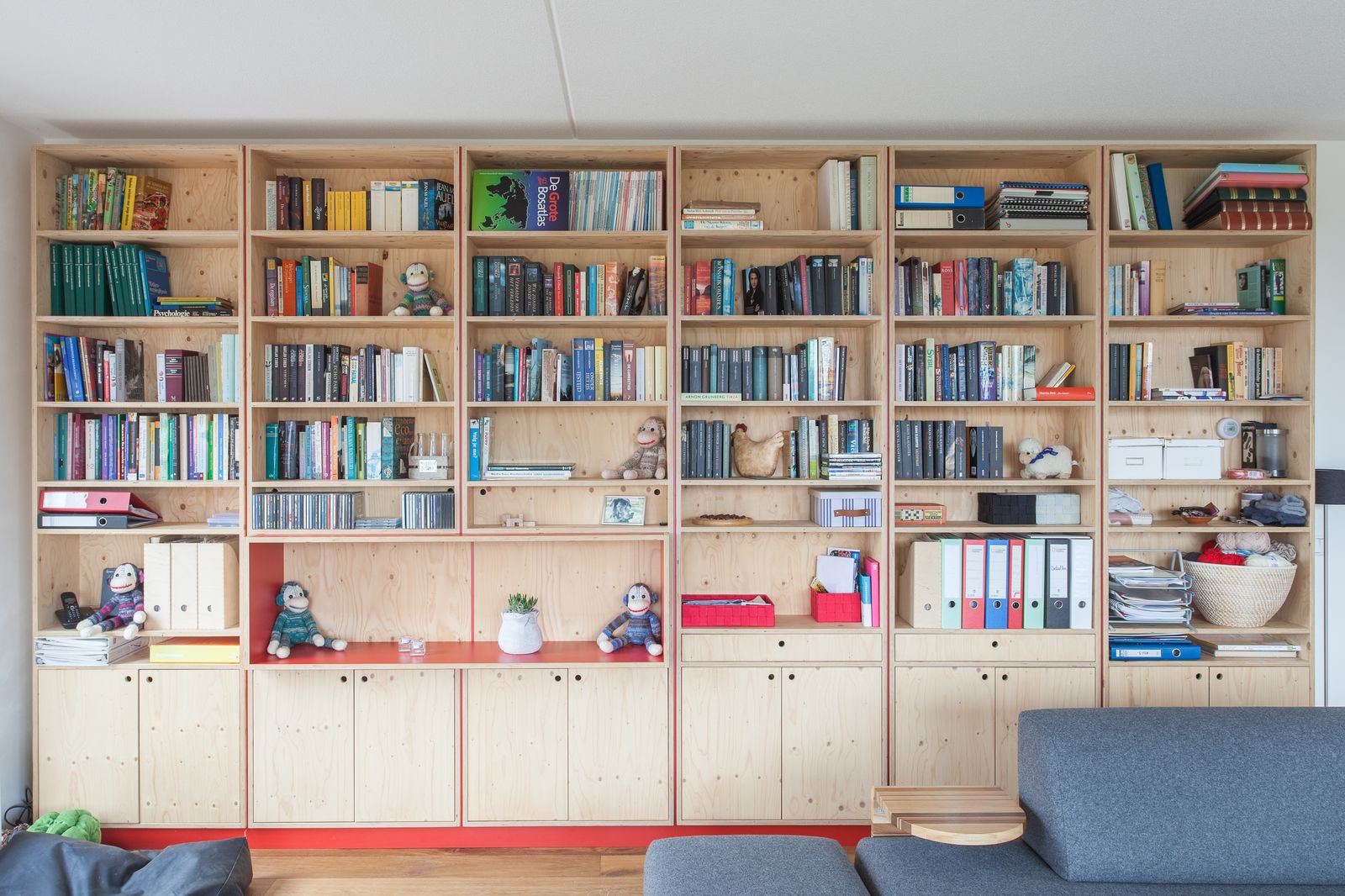 Wandvullende boekenkast van hout met rode achterwanden en open vakken vol boeken.
