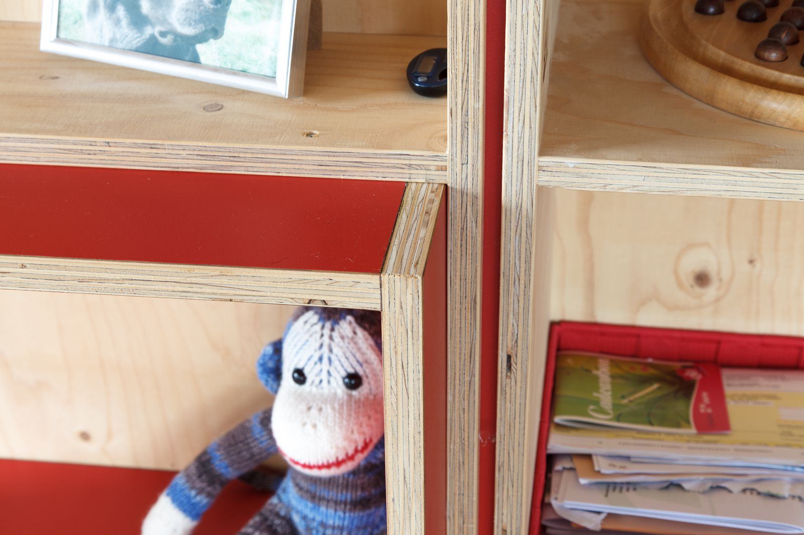 Detail van een houten kastvak met een fototijdklok, naast een rode achterwand.