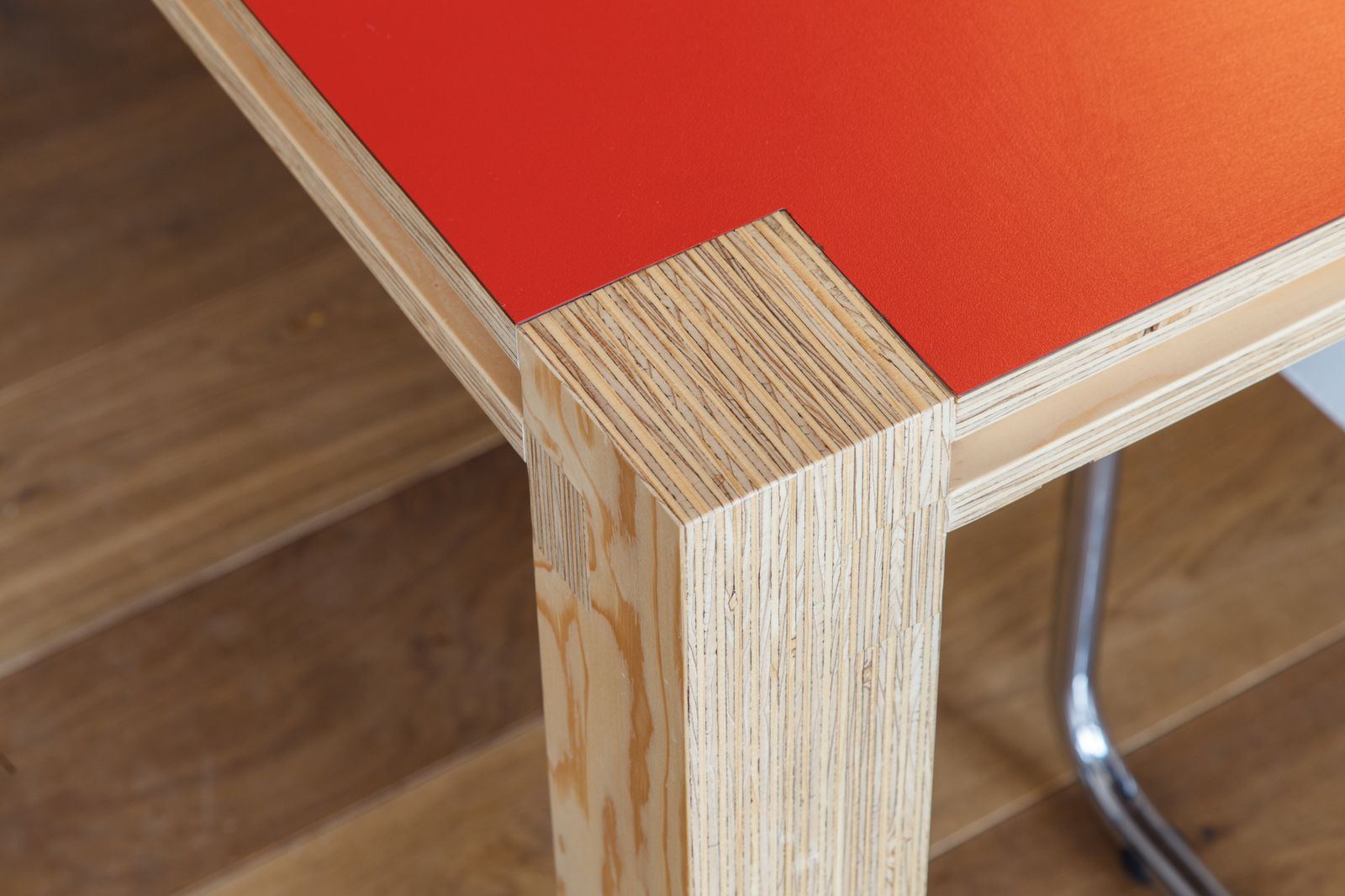 Detail van de hoek waar een houten tafelpoot het rode tafelblad ondersteunt.