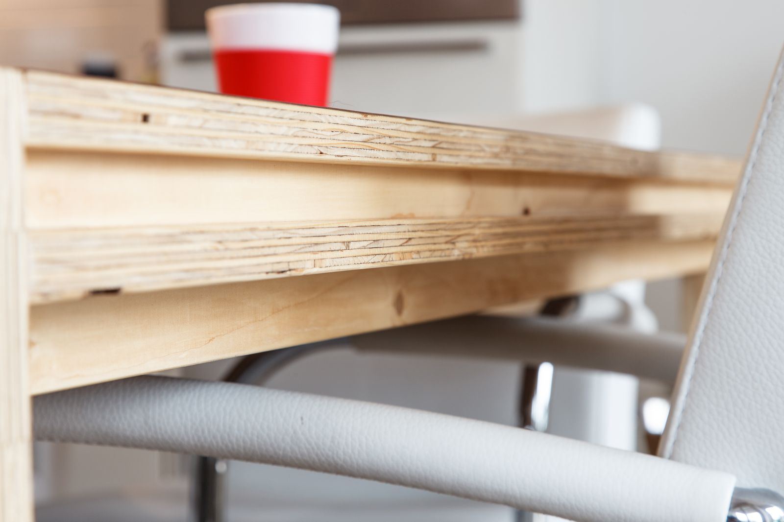 Detail van de dikke, houten rand van een tafel, met stoelen eronder.