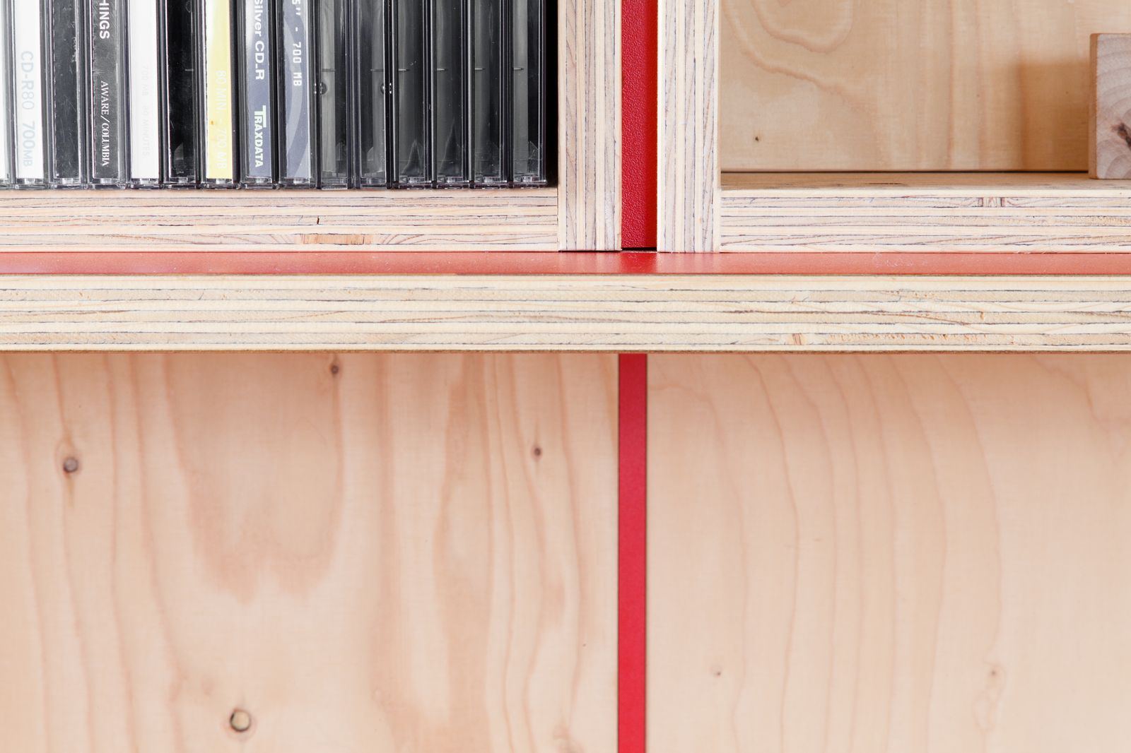 Detail van een rode scheidingsstrook tussen twee kastvakken, met cd's op de plank.