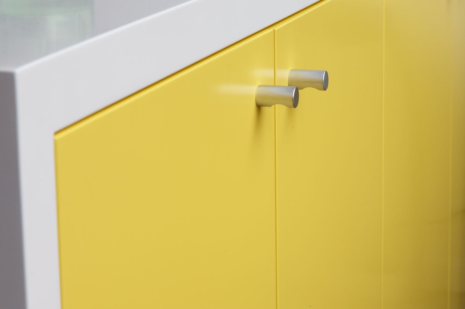 Close-up van twee ronde aluminium deurknopjes op een geel front.