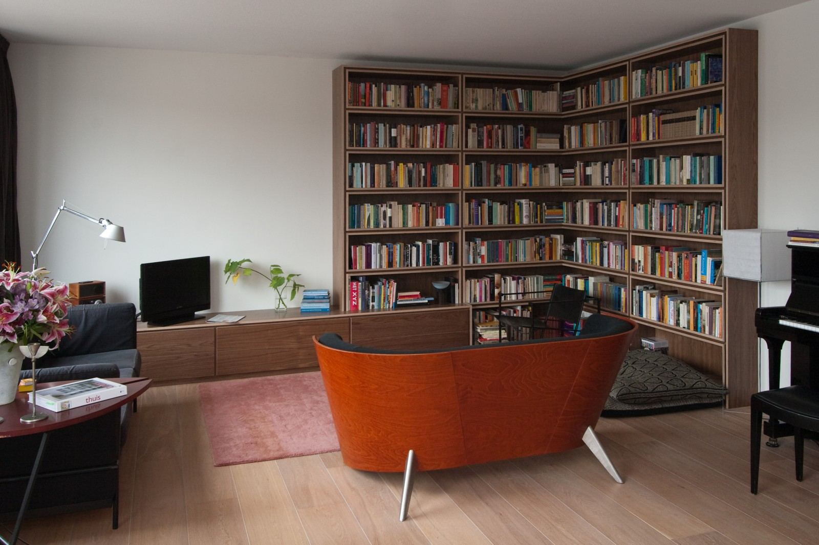 Wandvullende boekenkast die om een hoek heen loopt, boven een lage kast met een televisie.