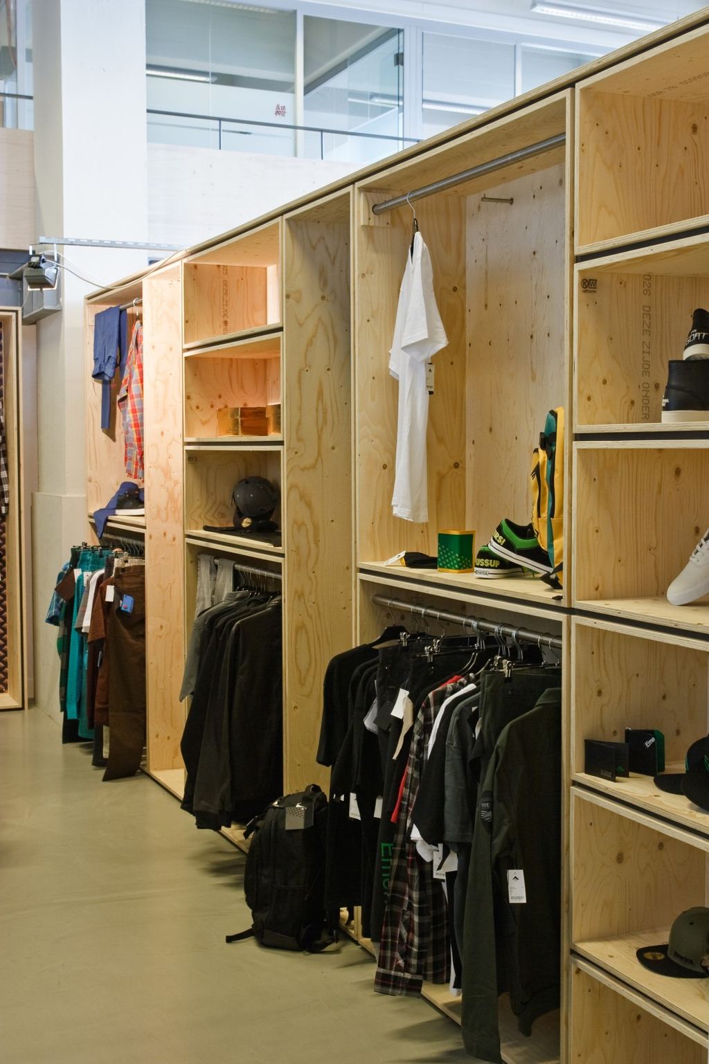 Lange vuren multiplex stellingwand met kledingrekken en schoenenvakken.