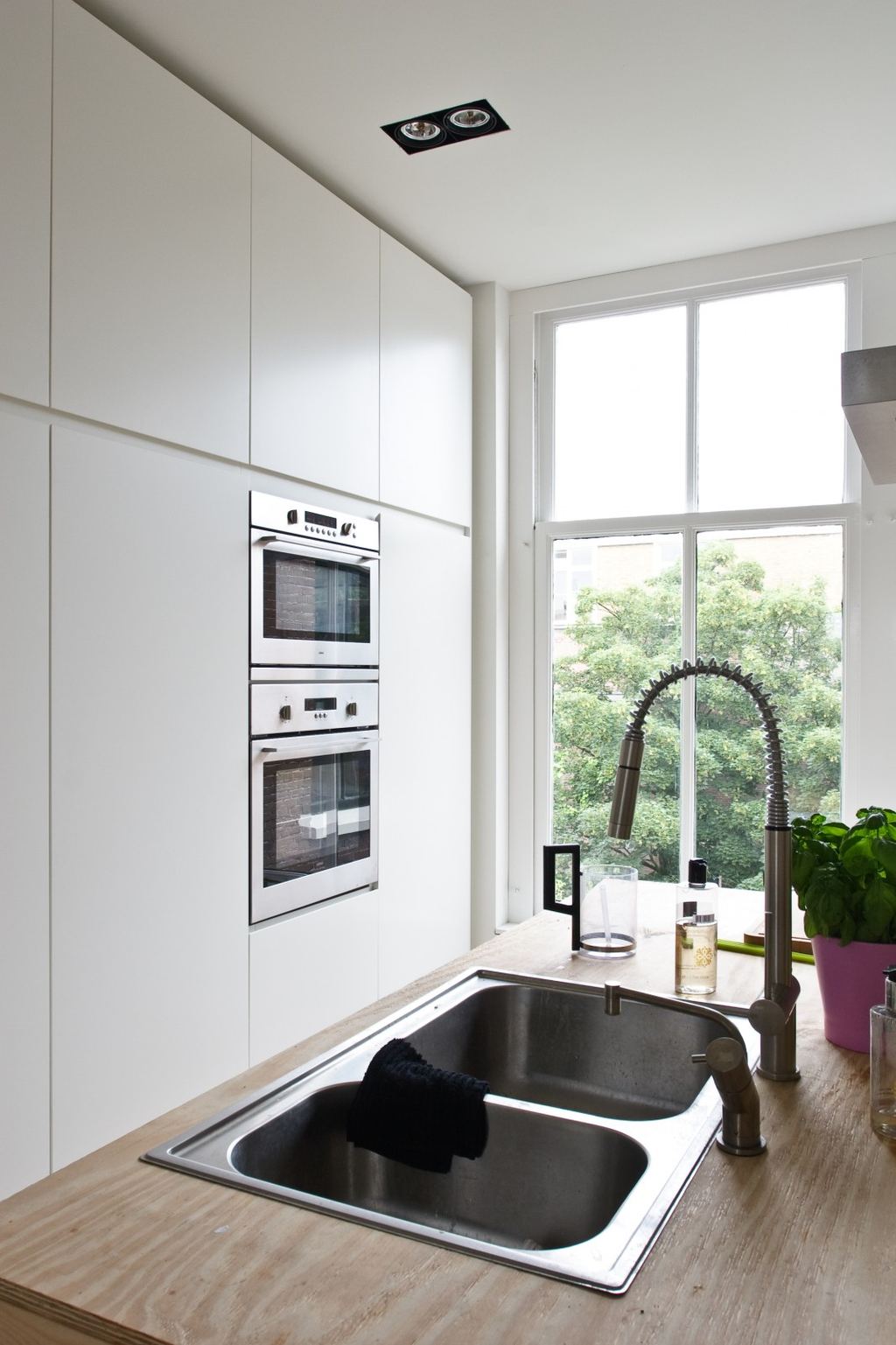 Witte keukenkasten met een dubbele oven boven een spoelbak met vuren blad.
