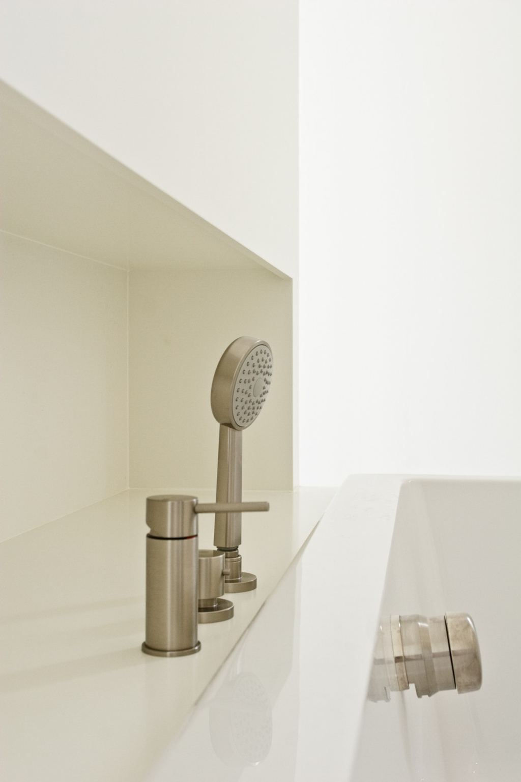 Detail van de witte badombouw met inbouwkraan en handdouche.