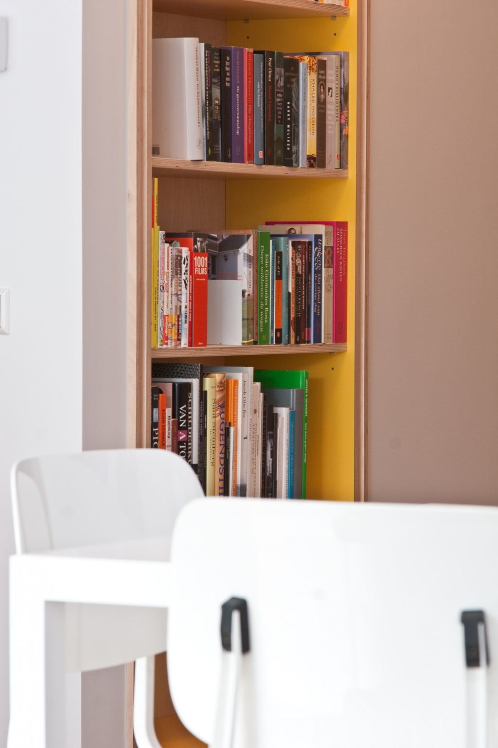 Detail van de boekenplanken met een felgele achterwand erachter.