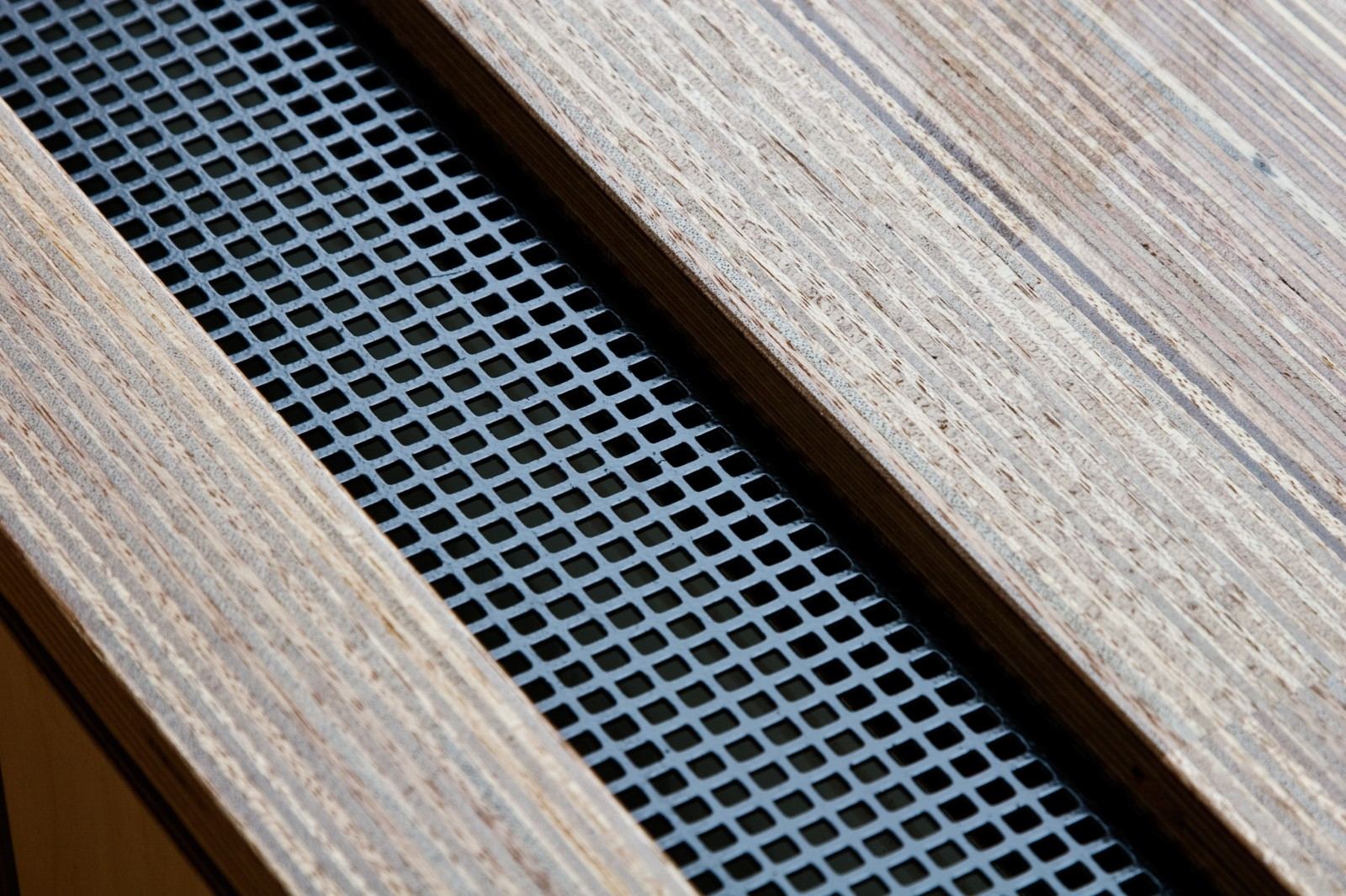 Extreme close-up van de geperforeerde metalen strook tussen twee houten panelen.
