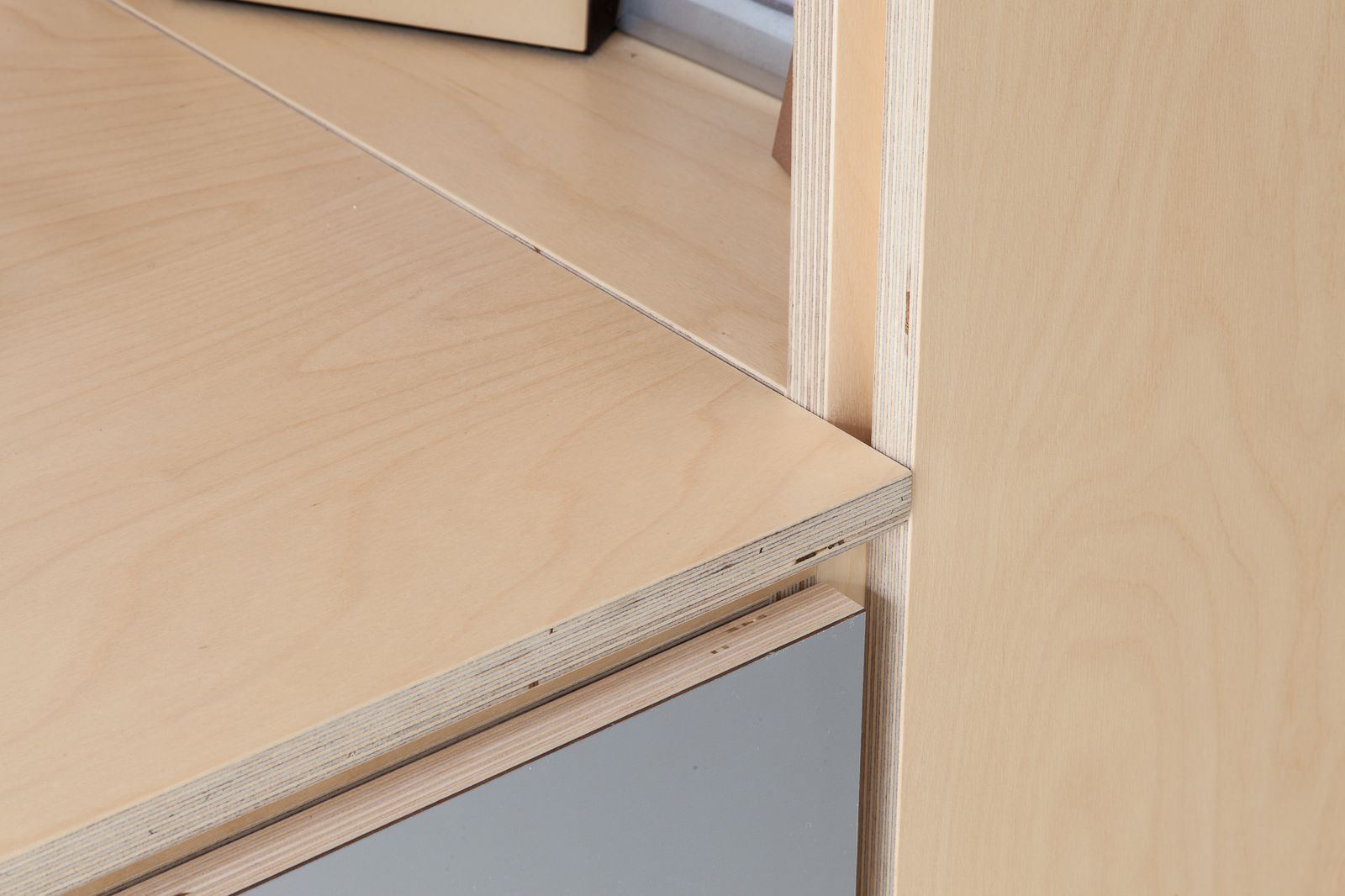 Detail van de constructie waar een berken schap een grijs front raakt.