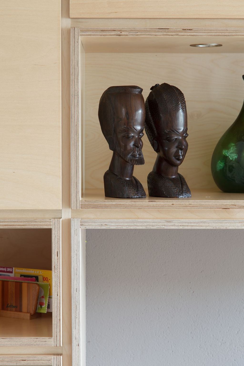 Detail van een display-nis met twee gebeeldhouwde houten bustes en een groene glazen vaas.