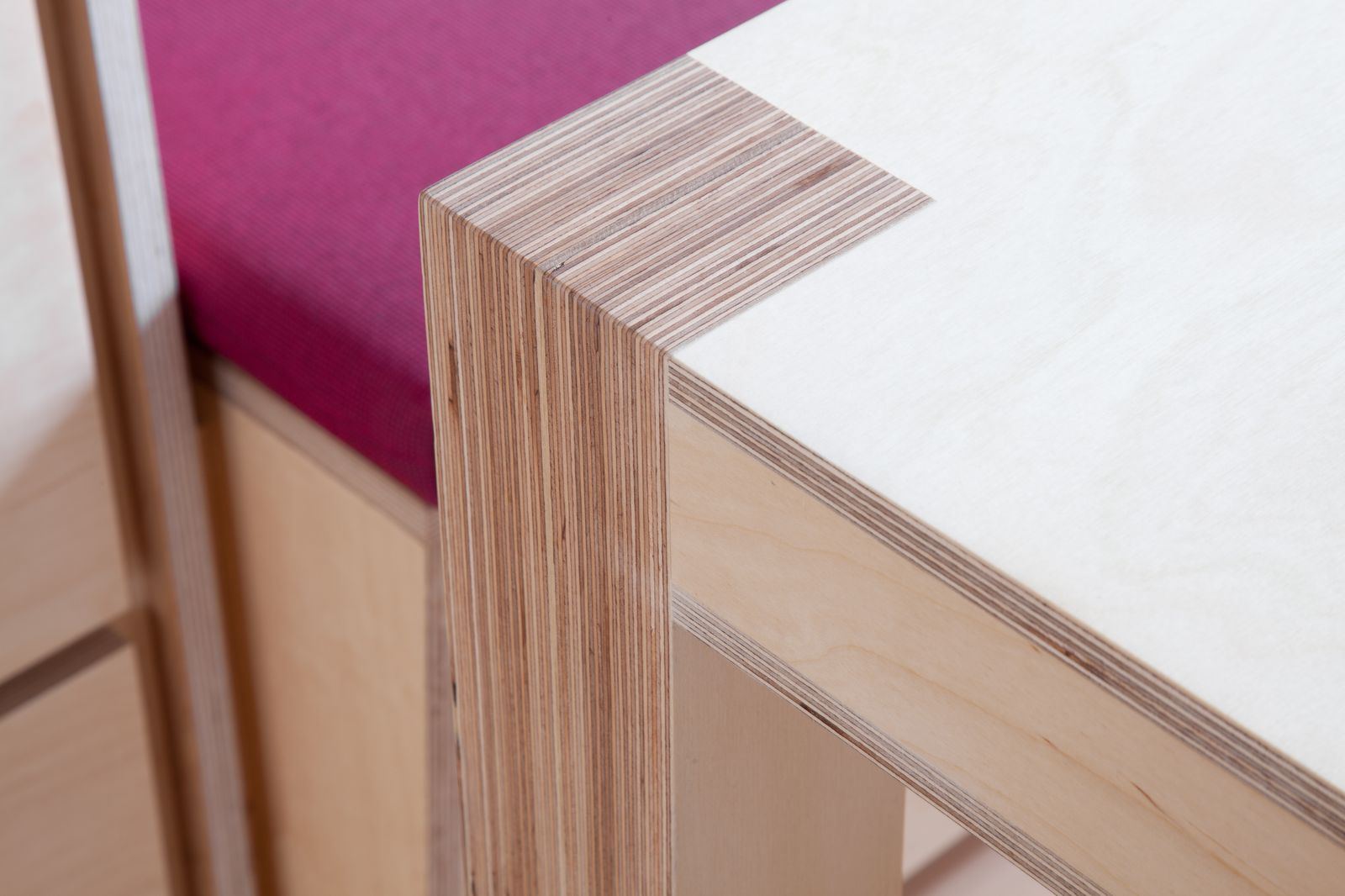 Detail van de hoek van een tafelblad met plaatrand, naast een roze zitkussen.