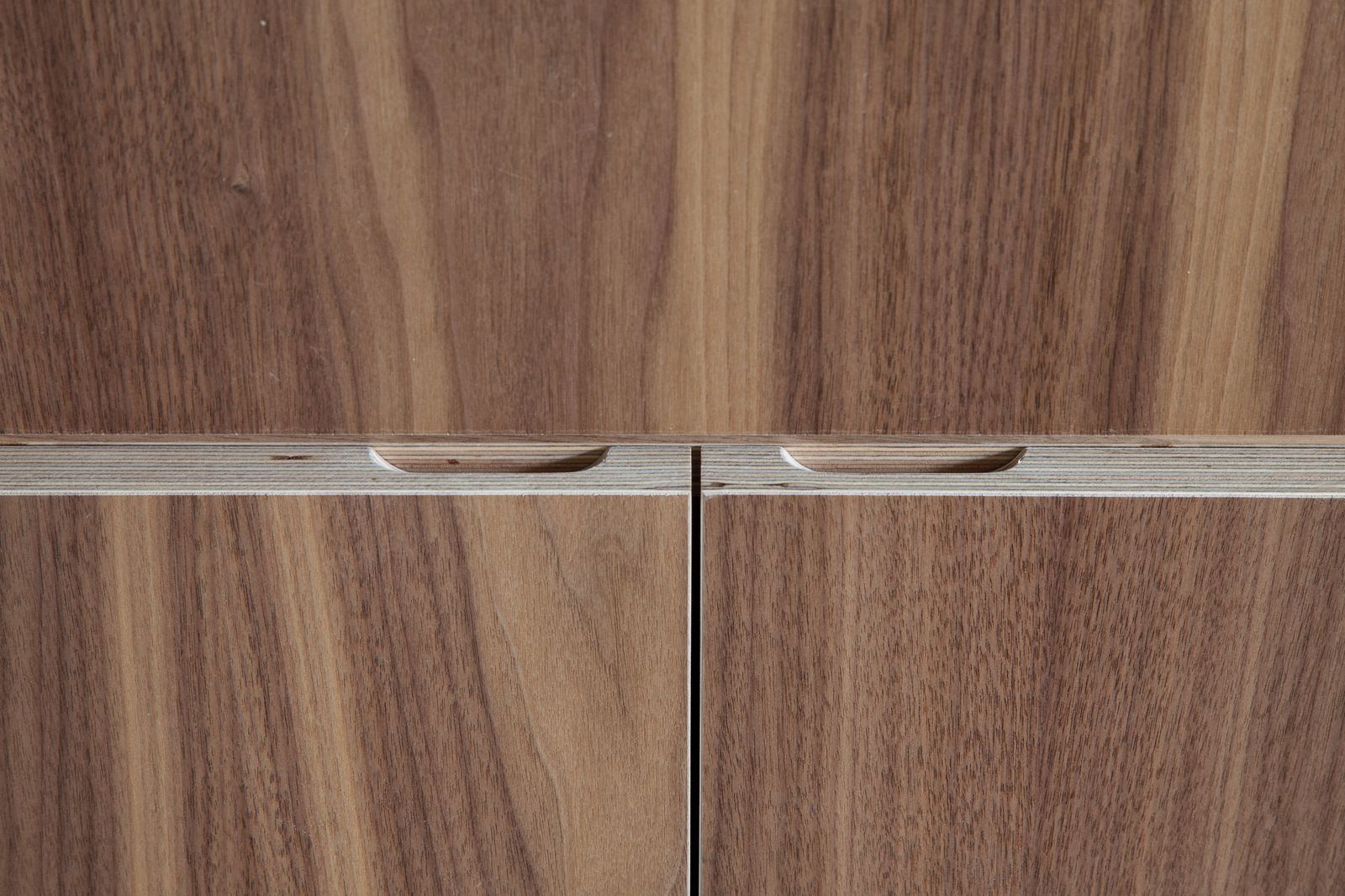 Detail van de gefreesde greep tussen twee notenhouten kastdeuren.