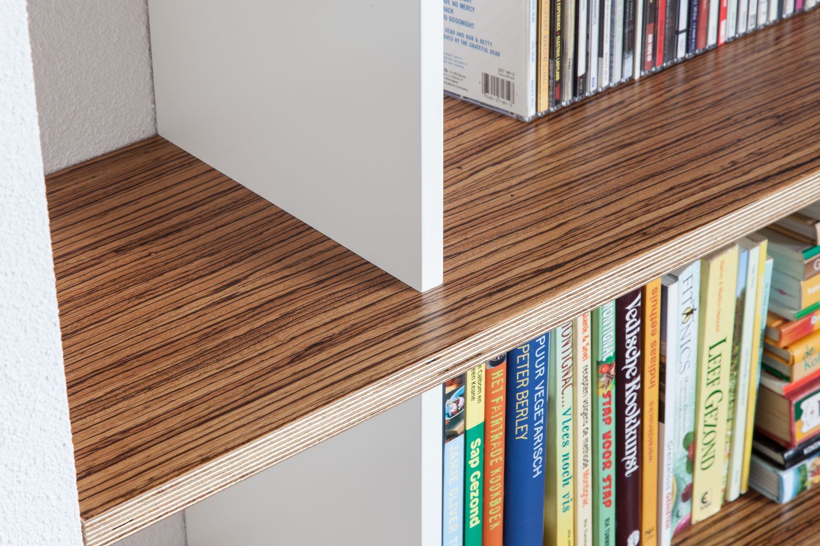 Detail van een gestreepte houten plank, met cd's erboven en kookboeken eronder.