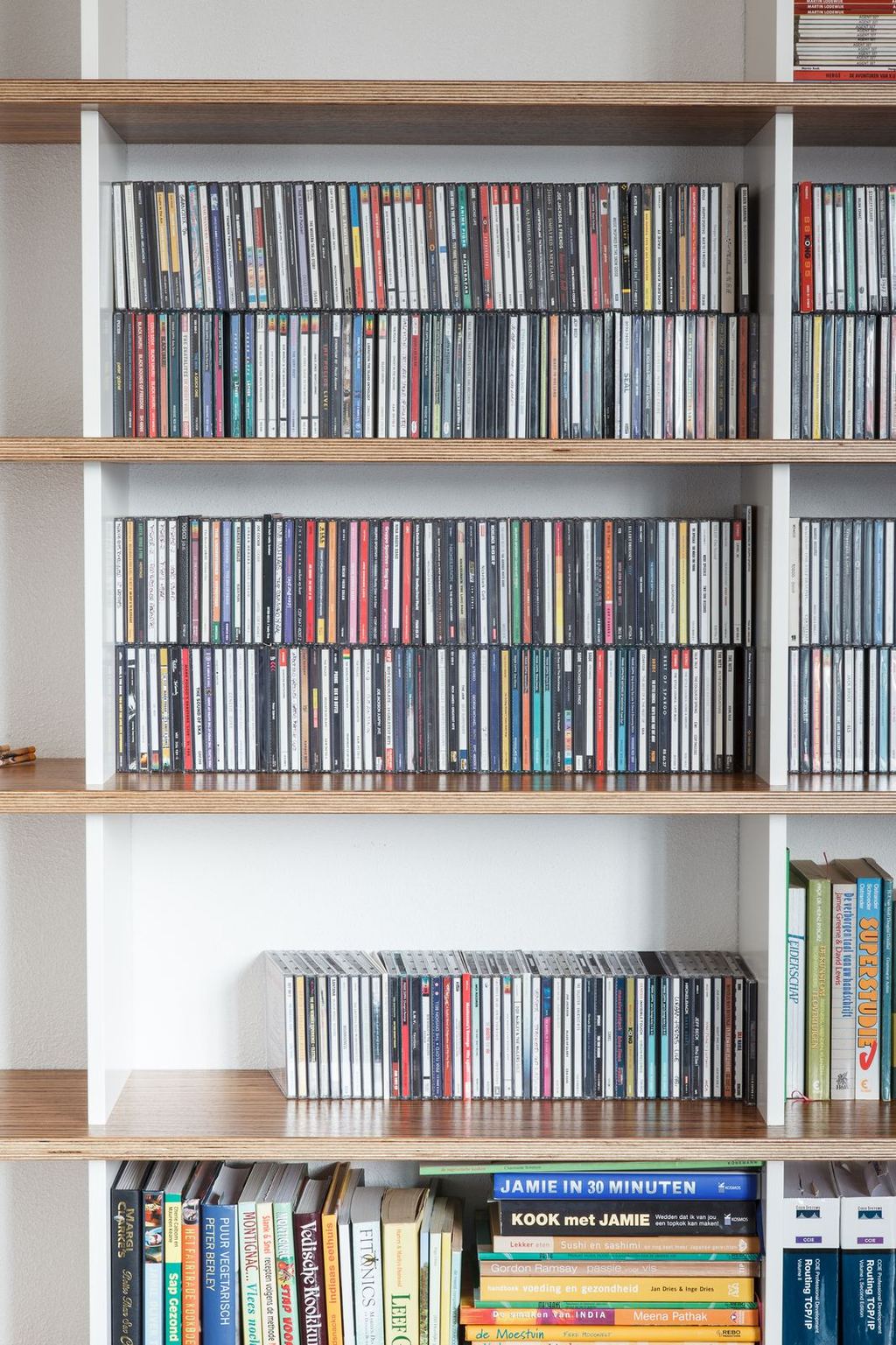 Boekenplank volledig gevuld met cd's, met kookboeken op de plank eronder.
