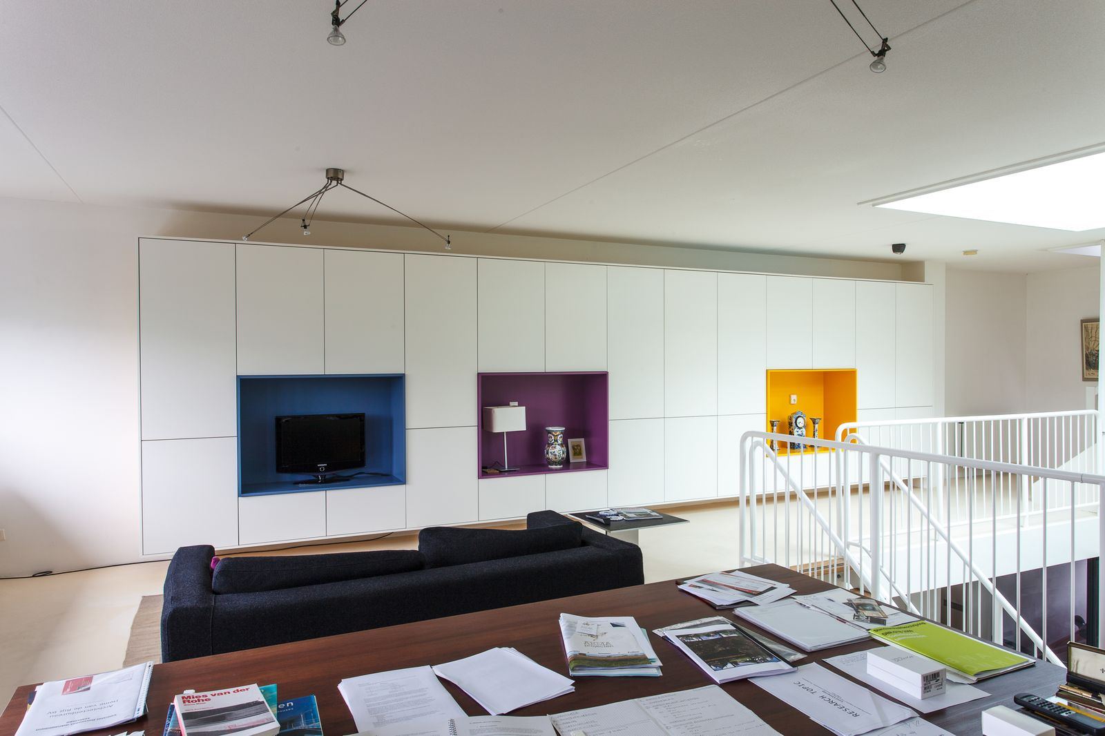 Lange witte kastenwand met kleurrijke nissen voor televisie en vaas.