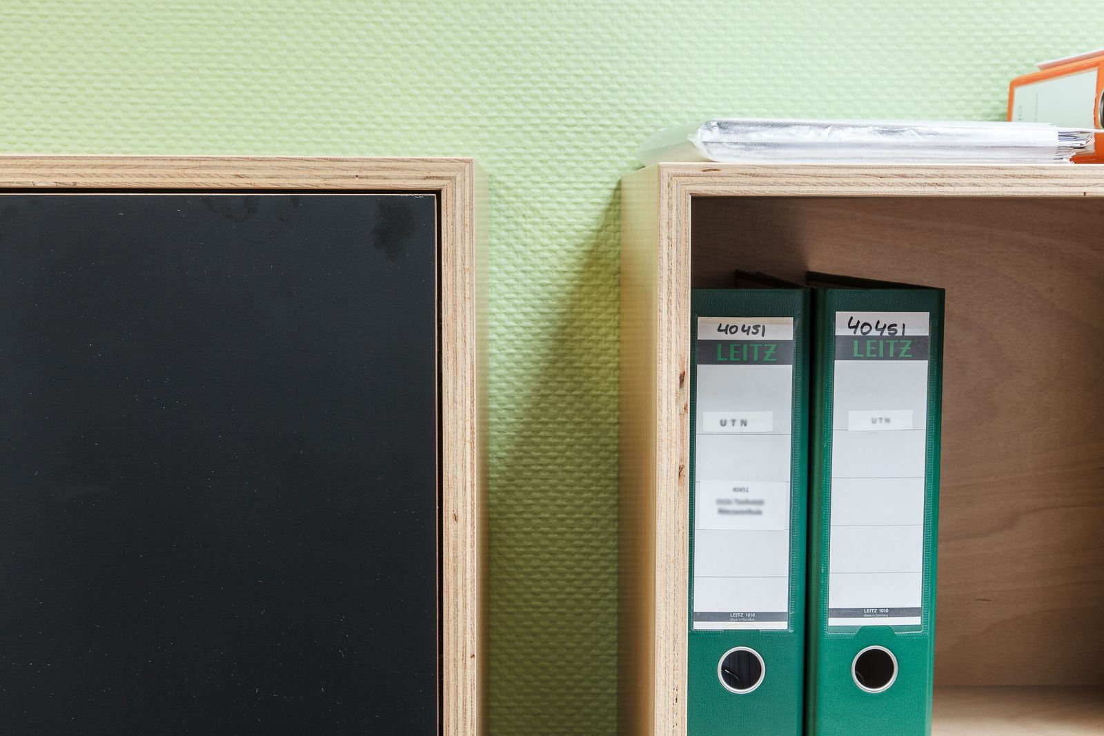 Zwart kastfront naast een open vak met groene ordners.