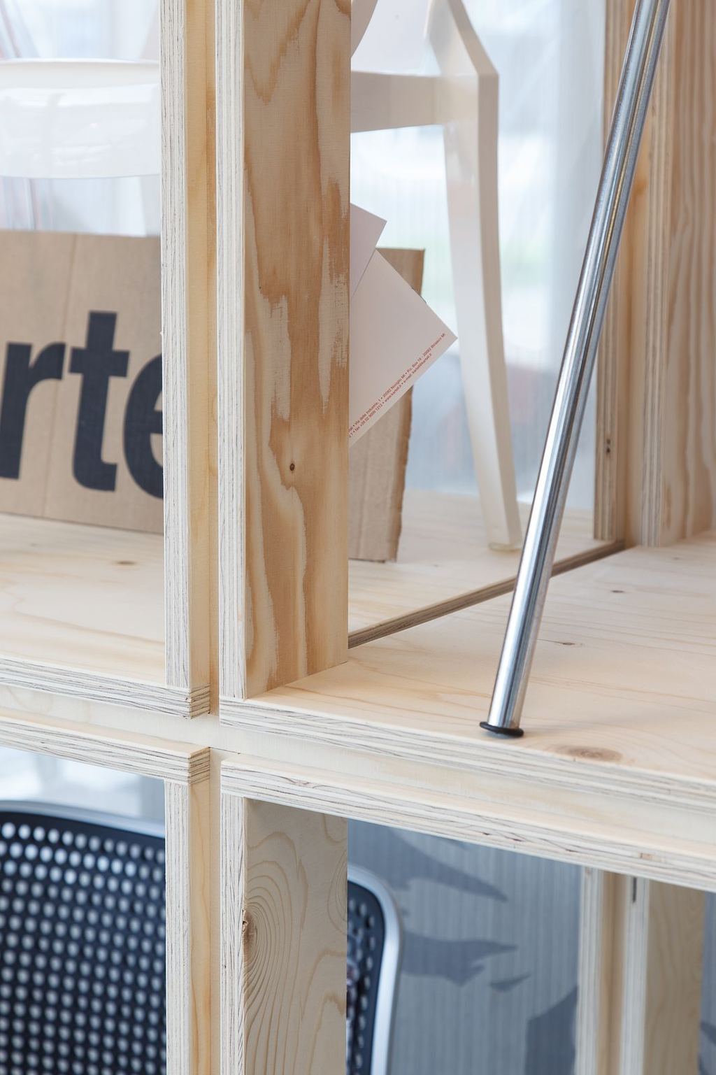 Detailopname van de houten hoekverbinding van het rek, met een kaartje tussen de planken.