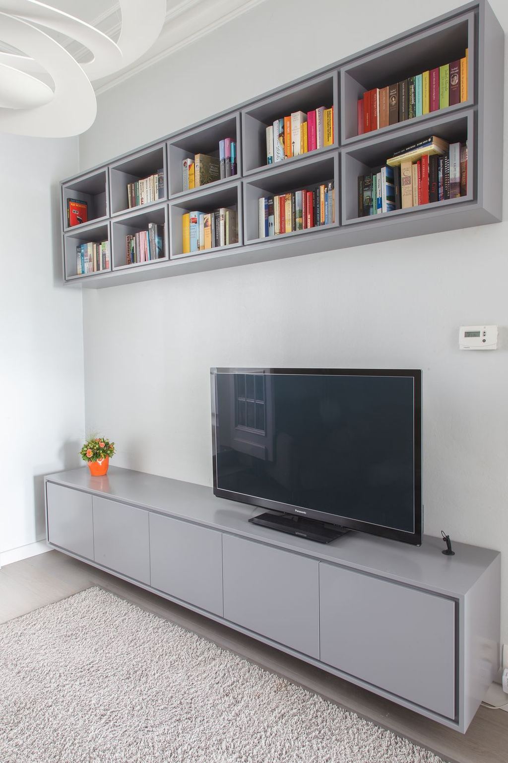 Zwevende grijze boekenkast boven een even grijs tv-dressoir.