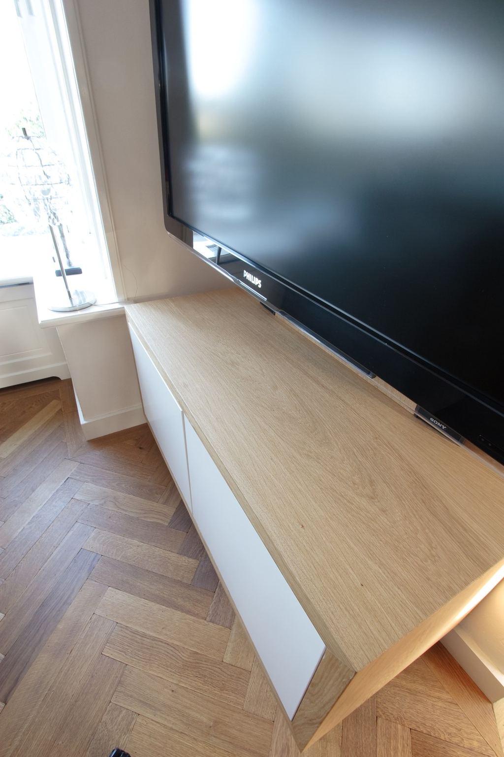 Close-up van een zwevend tv-meubel met een licht houten blad en witte kastdeuren.