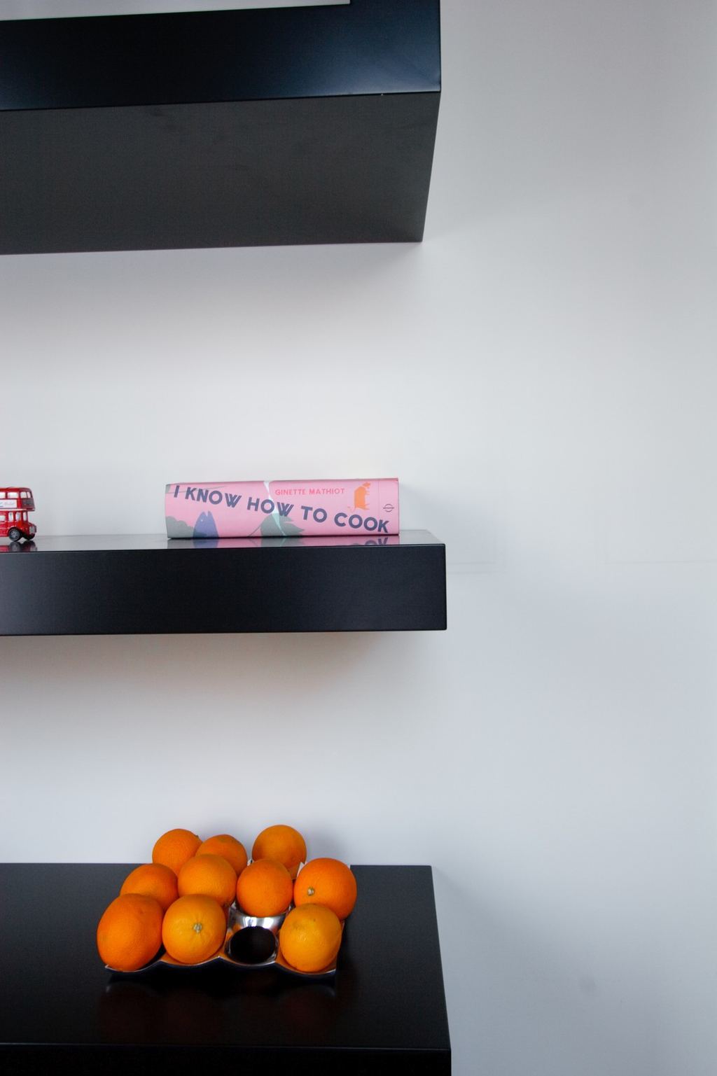 Detail van een zwarte plank met een boek en sinaasappels.